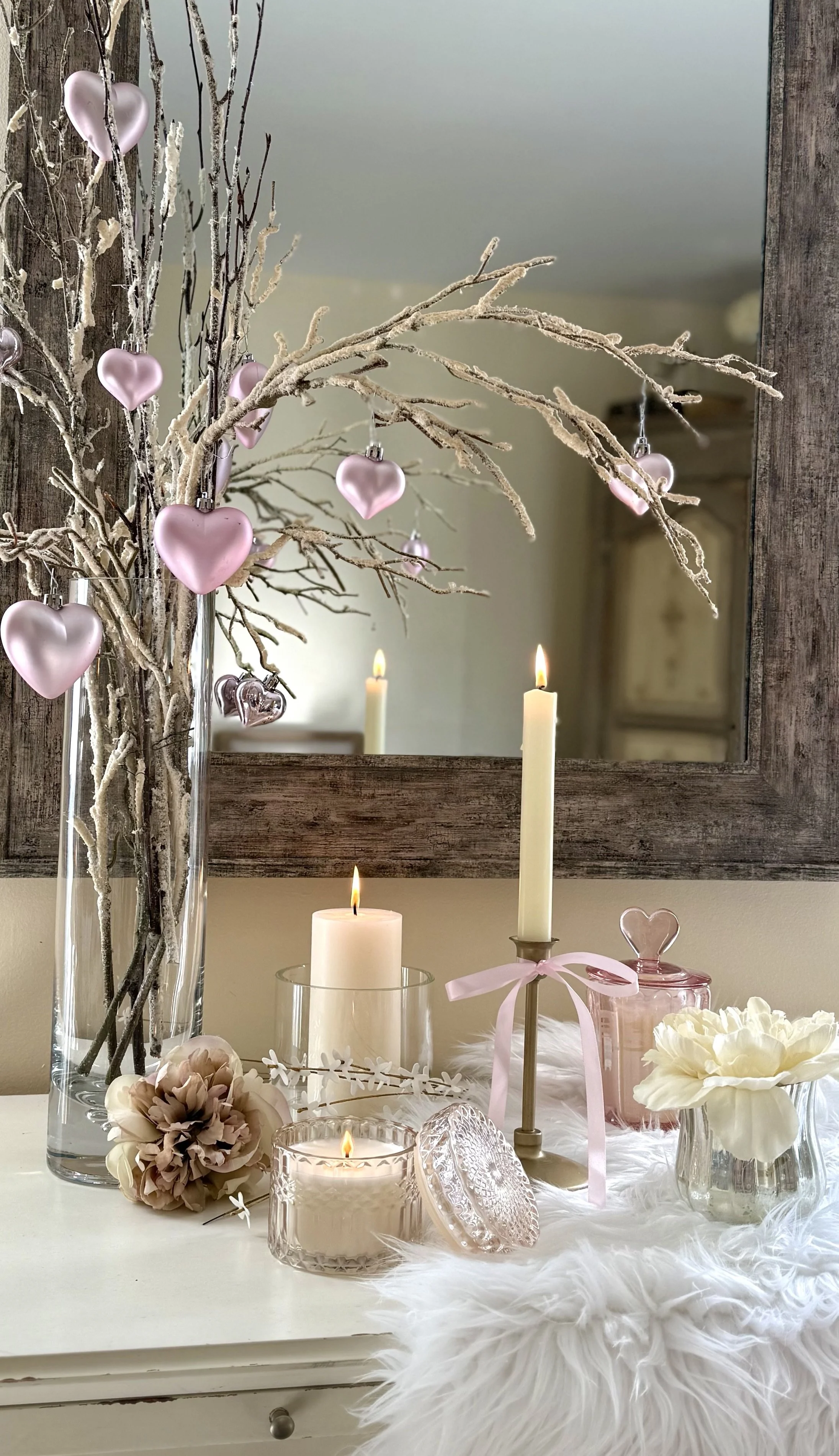Valentine's Day tabletop decor with pink heart ornaments, candles, soft florals, and romantic accents including a distressed wooden mirror which adds contrast to the softness of the pink and white.