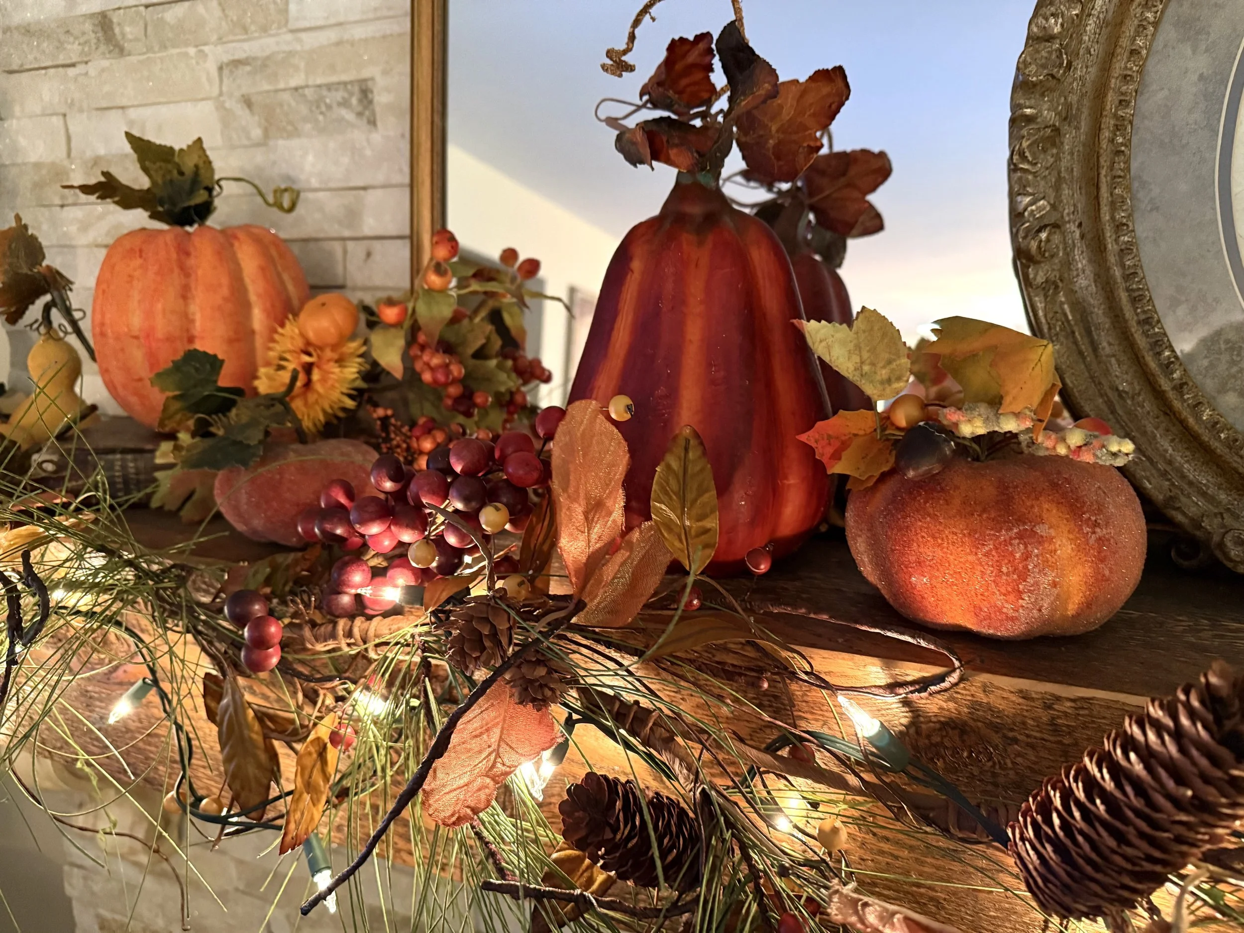 Autumn fall decorations including pumpkins, grapevine, and leaves on a wooden surface with a mirror and wall in the background.