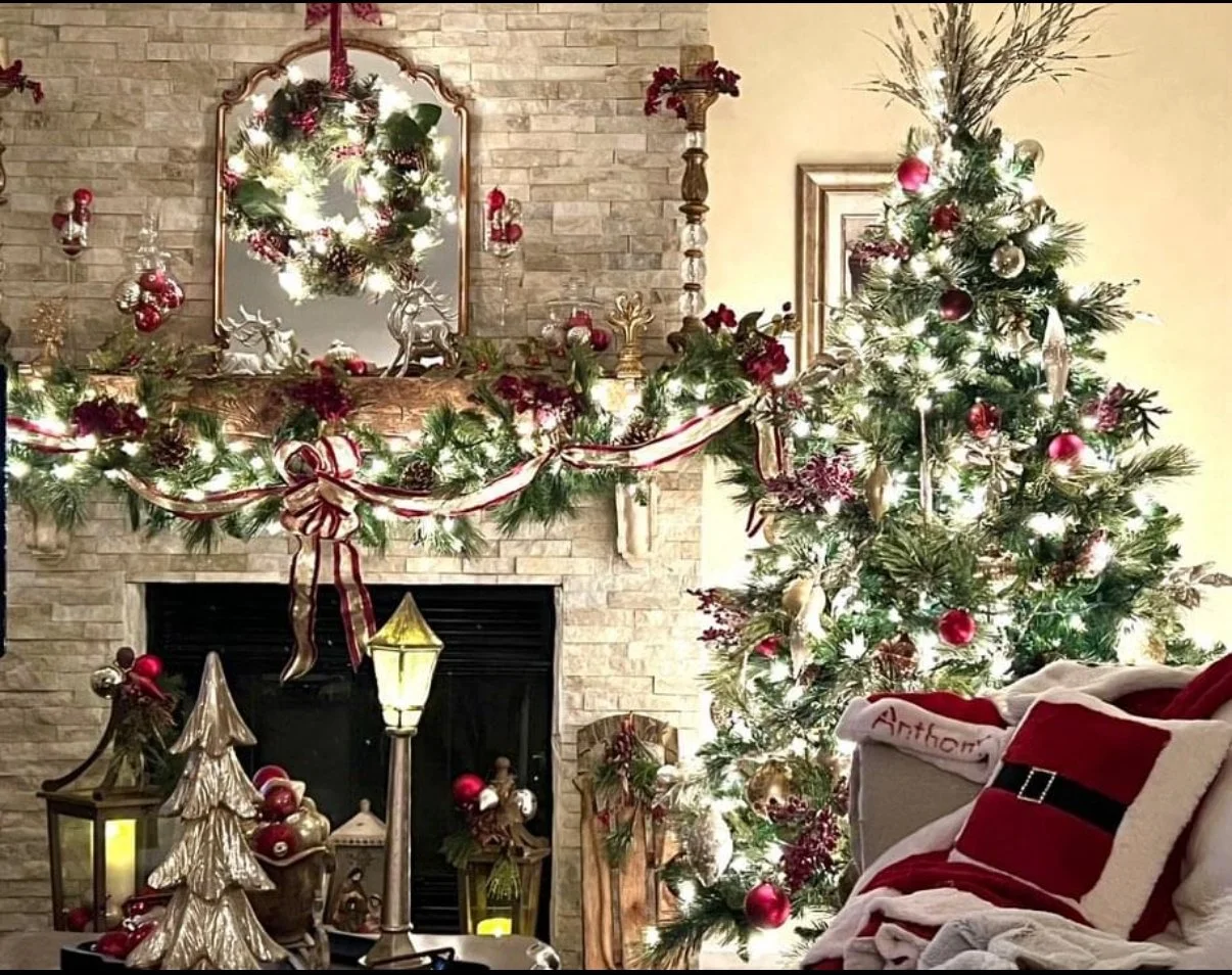 Decorated Christmas living room with a lit Christmas tree, festive garland, and ornaments, along with a fireplace, lanterns, and a cozy chair with a Christmas pillow.