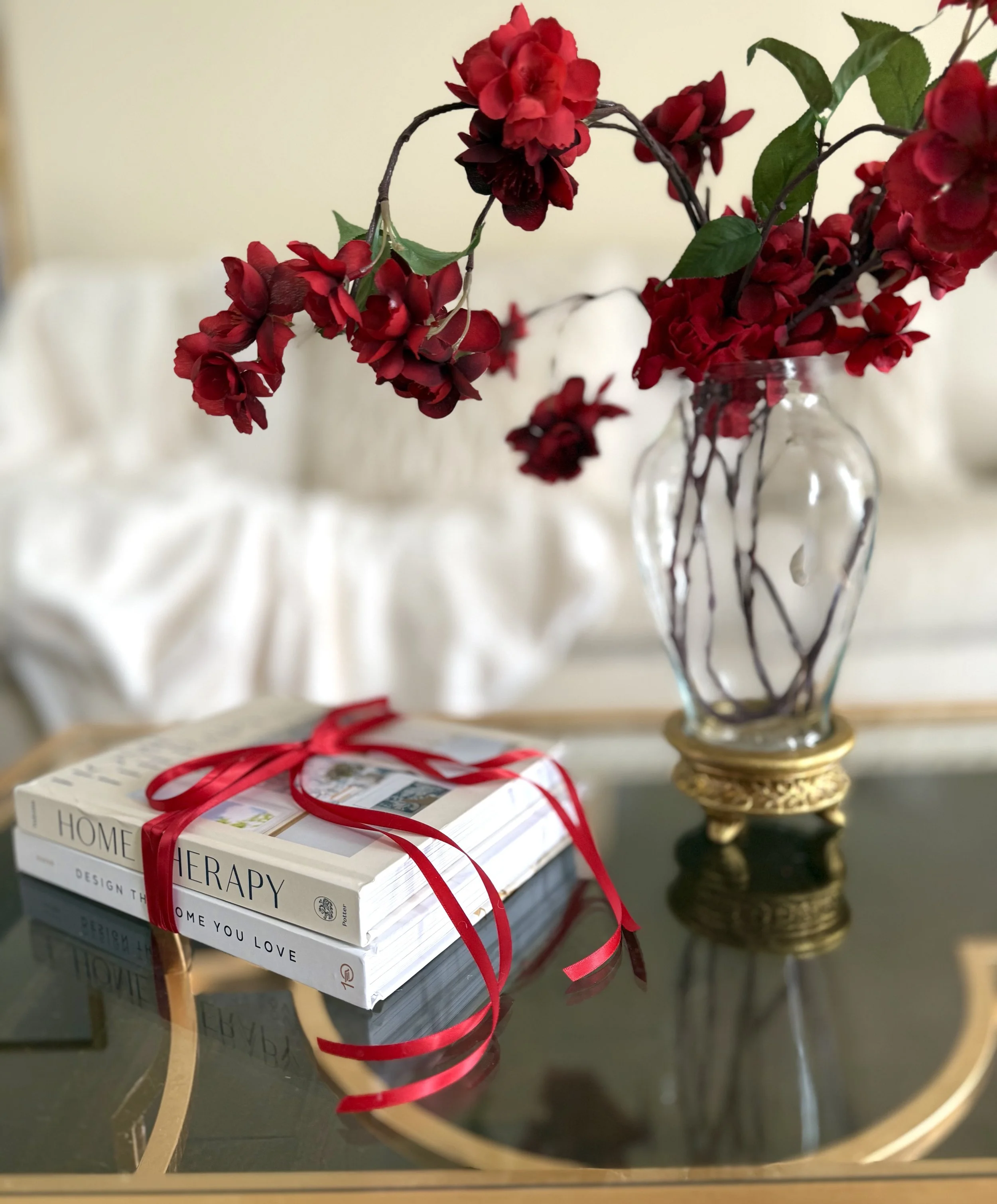 Valentine's Day decor makes a bold statement is made with these white books tied by a bright red bow on a gold coffee table next to a red flower arrangement in a clear glass vase.
