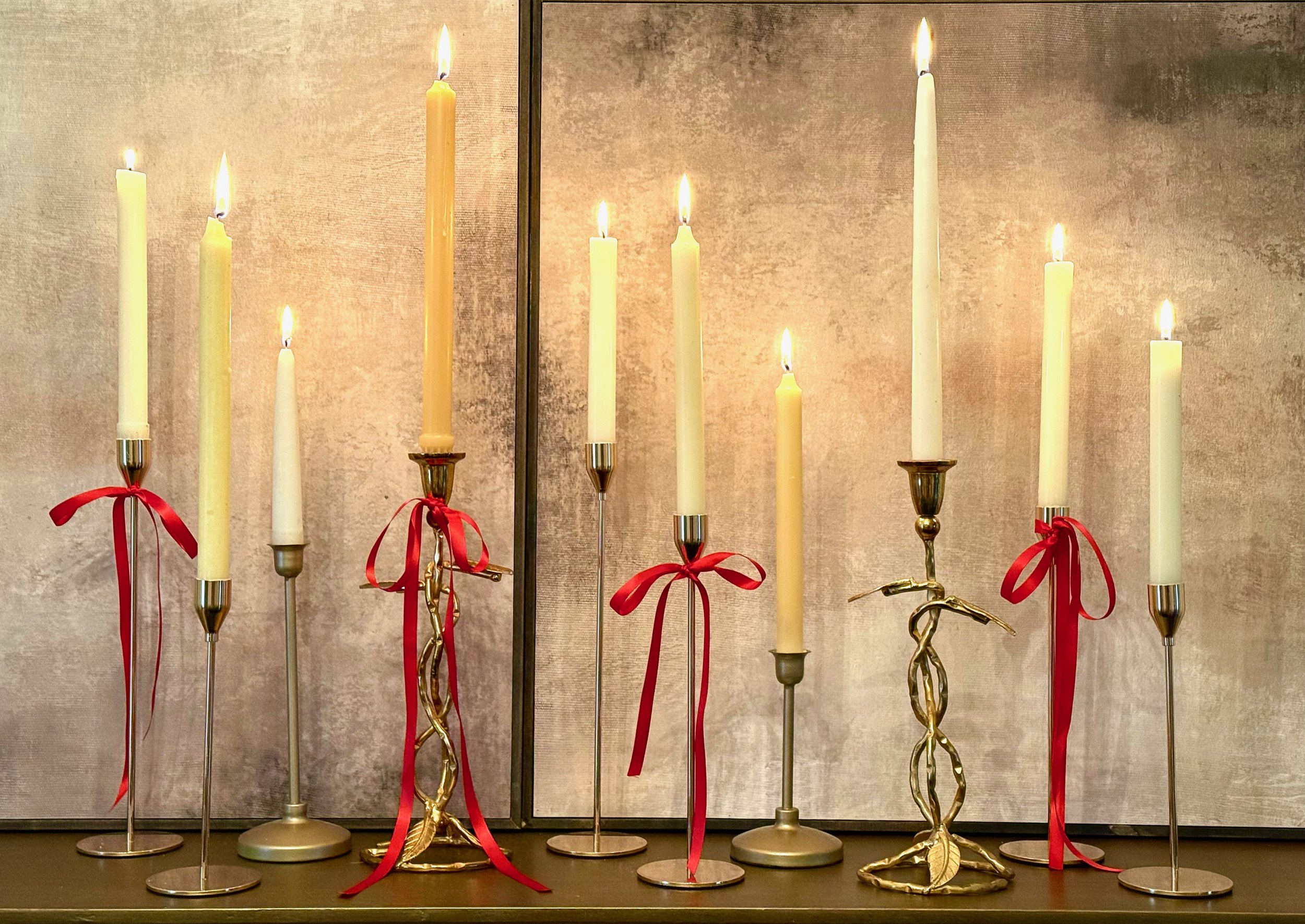 Valentine's Day candle sticks of various heights and styles tied with a thin red bow against a tan, brown and black background