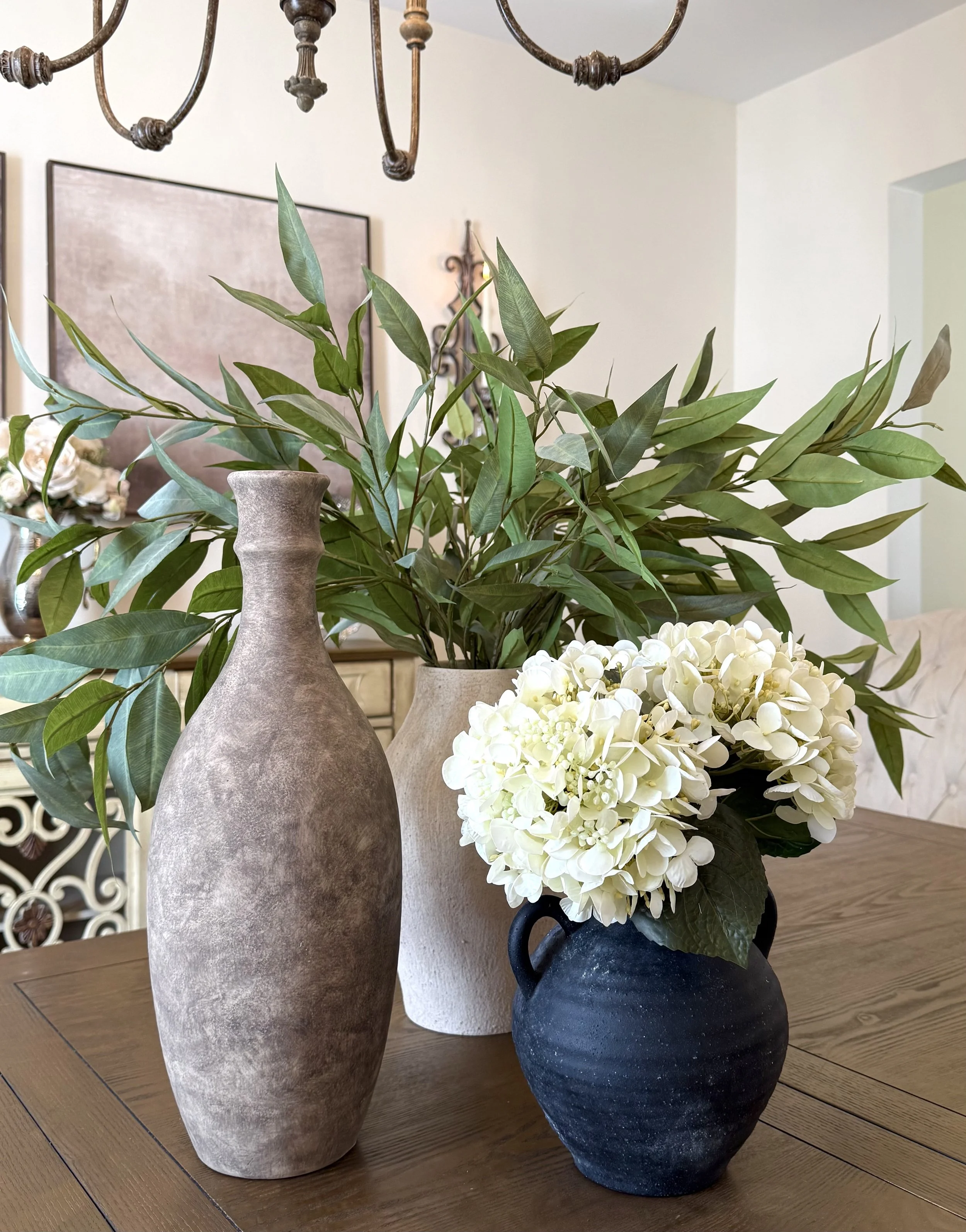 Styled dining room tyable featuring neutral and black ceramic vases, white florals, and greenery for a timeless, elegant look.