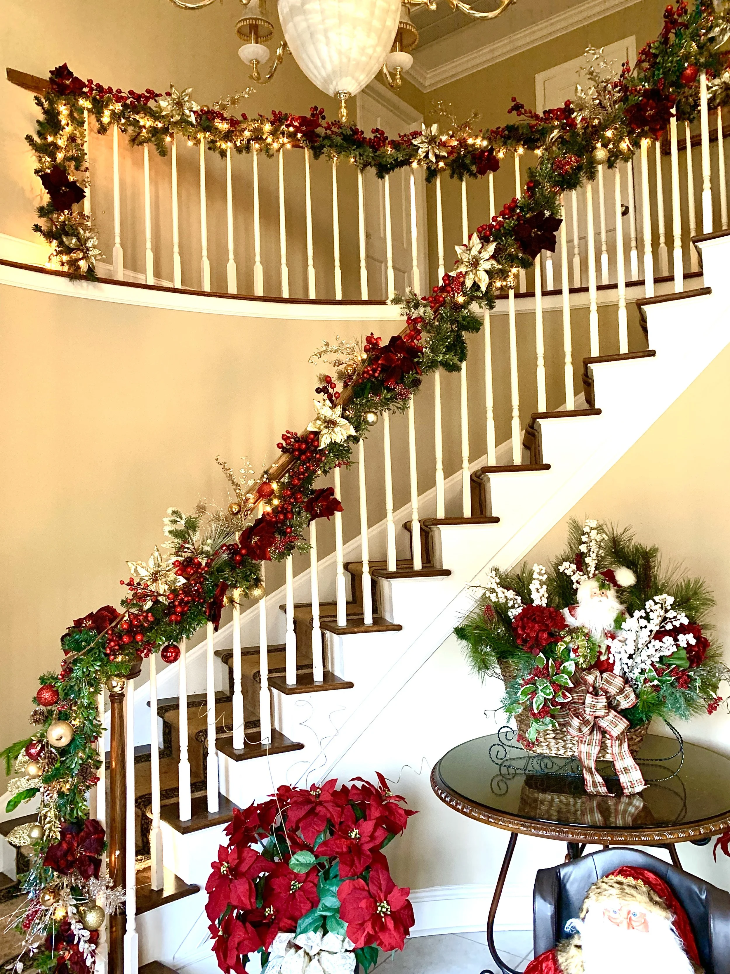 Decorated staircase with Christmas garland and poinsettia plant, along with festive holiday arrangement featuring Santa Claus figure on a table.