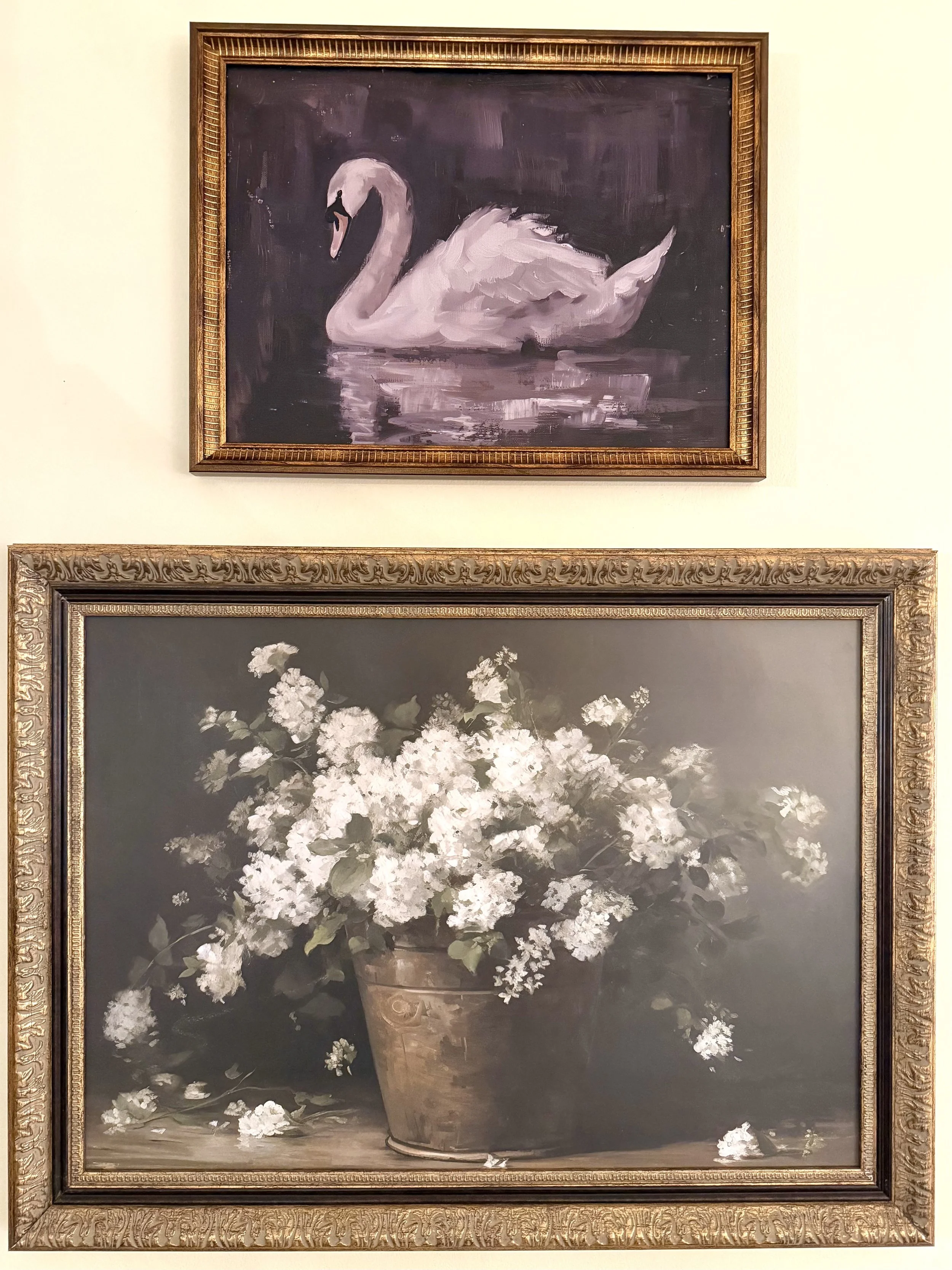 Two framed vintage artworks displayed vertically, featuring a swan painting above a floral still life, styled with warm tones and classic detailing. 