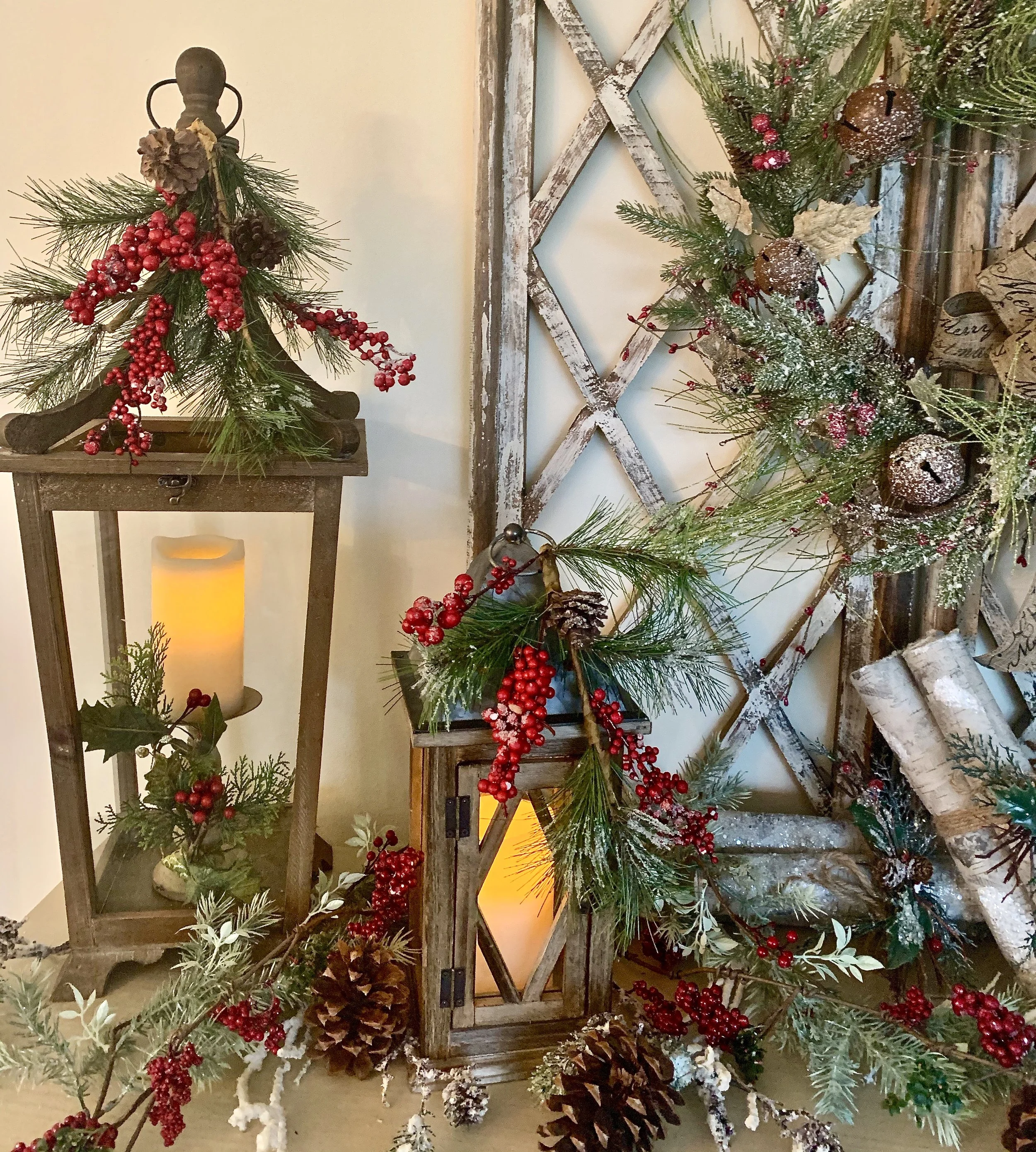 Decorative Christmas arrangement with greenery, red berries, cones, pinecones, and candles on wooden lanterns and a rustic wall hanger.