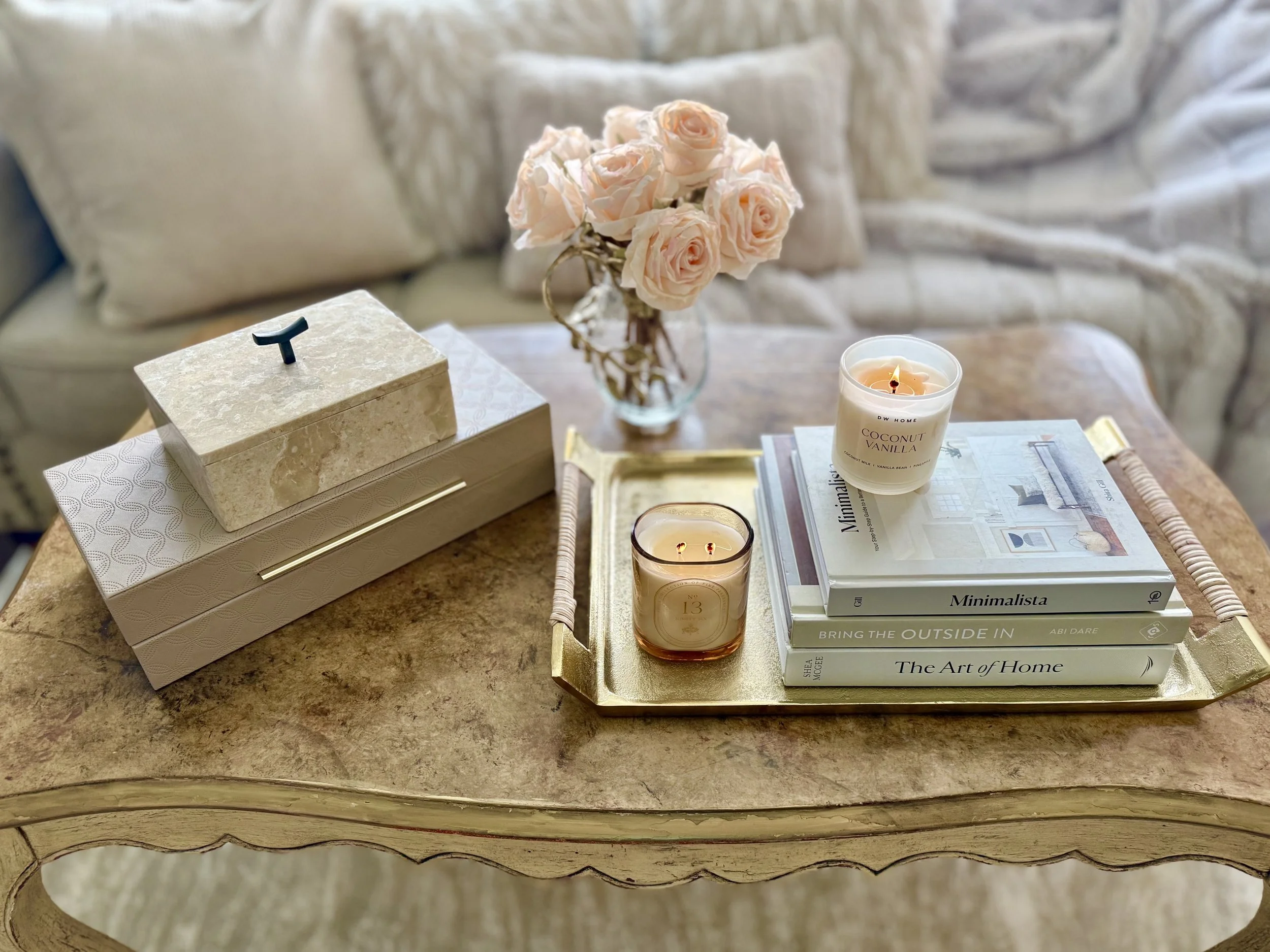 coffee table styling using stacked marble boxes, a gold tray with decorative books stacked on top with candles and a glass and gold jar filled with soft pink roses