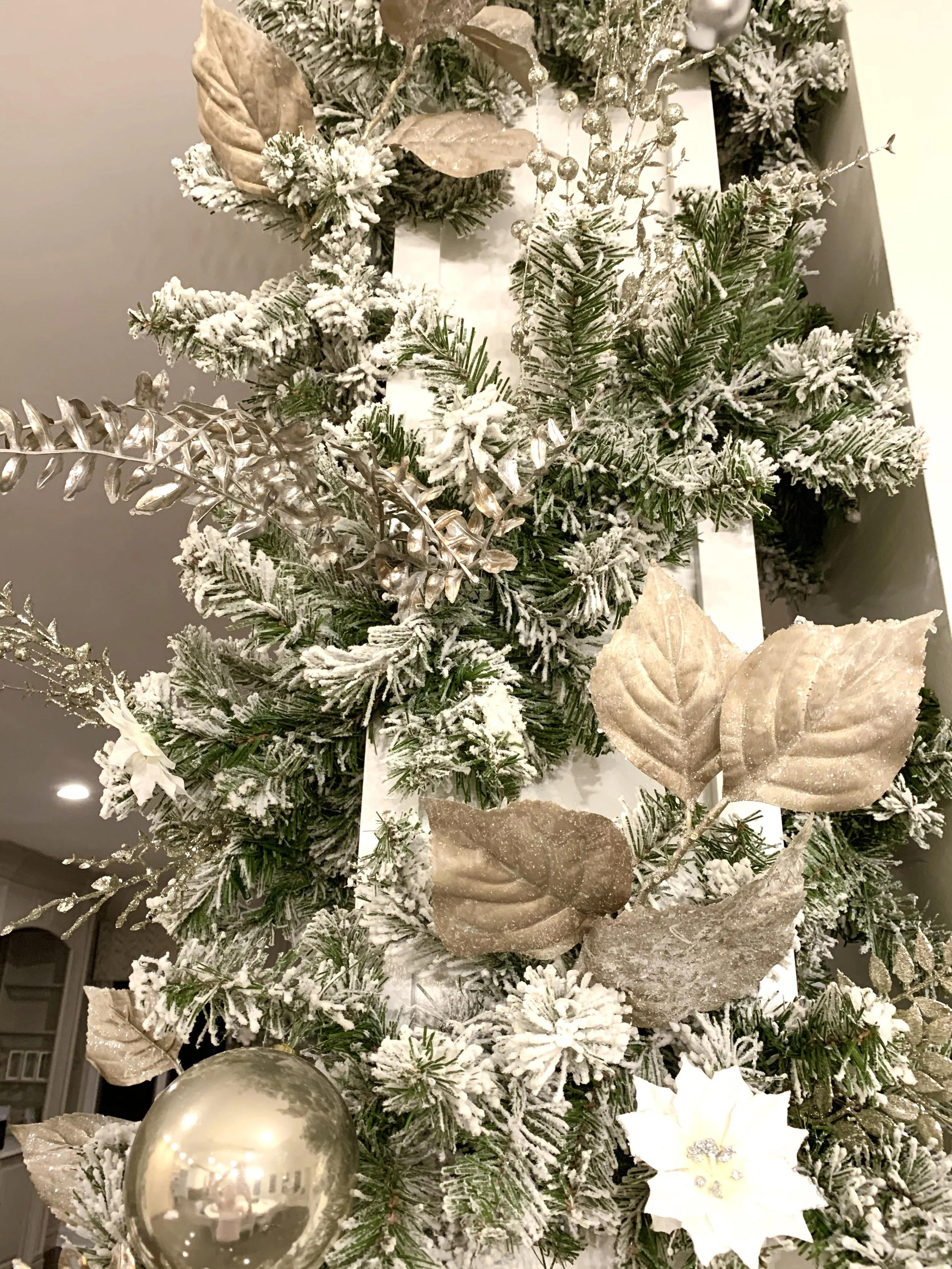 Close-up of a decorated Christmas tree with gold and white ornaments, frosted pine branches, and gold leaves.