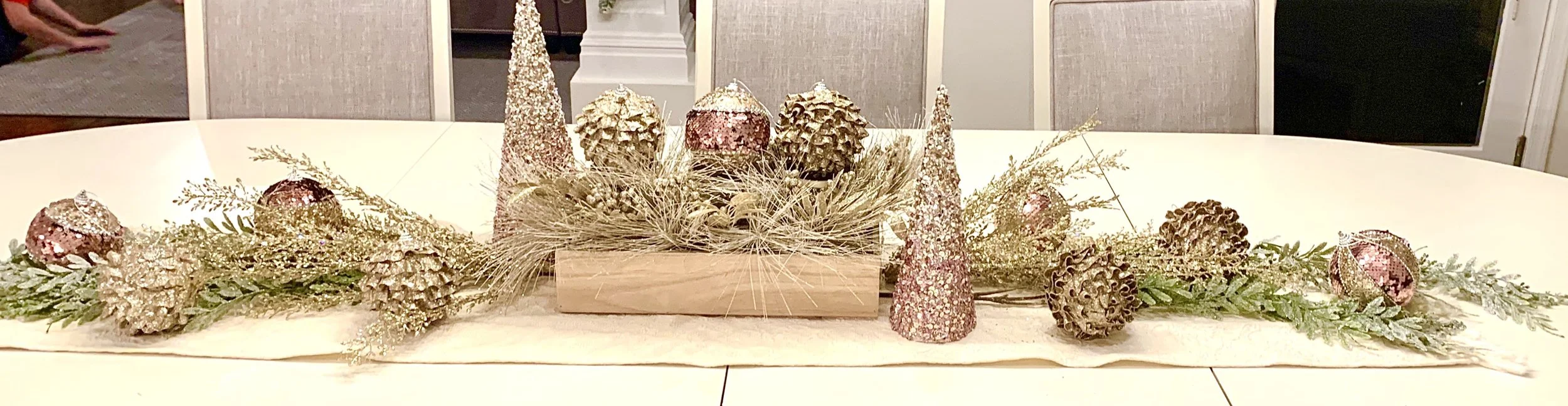 Decorative table runner with pinecones and glittery cone-shaped ornaments on a white table.