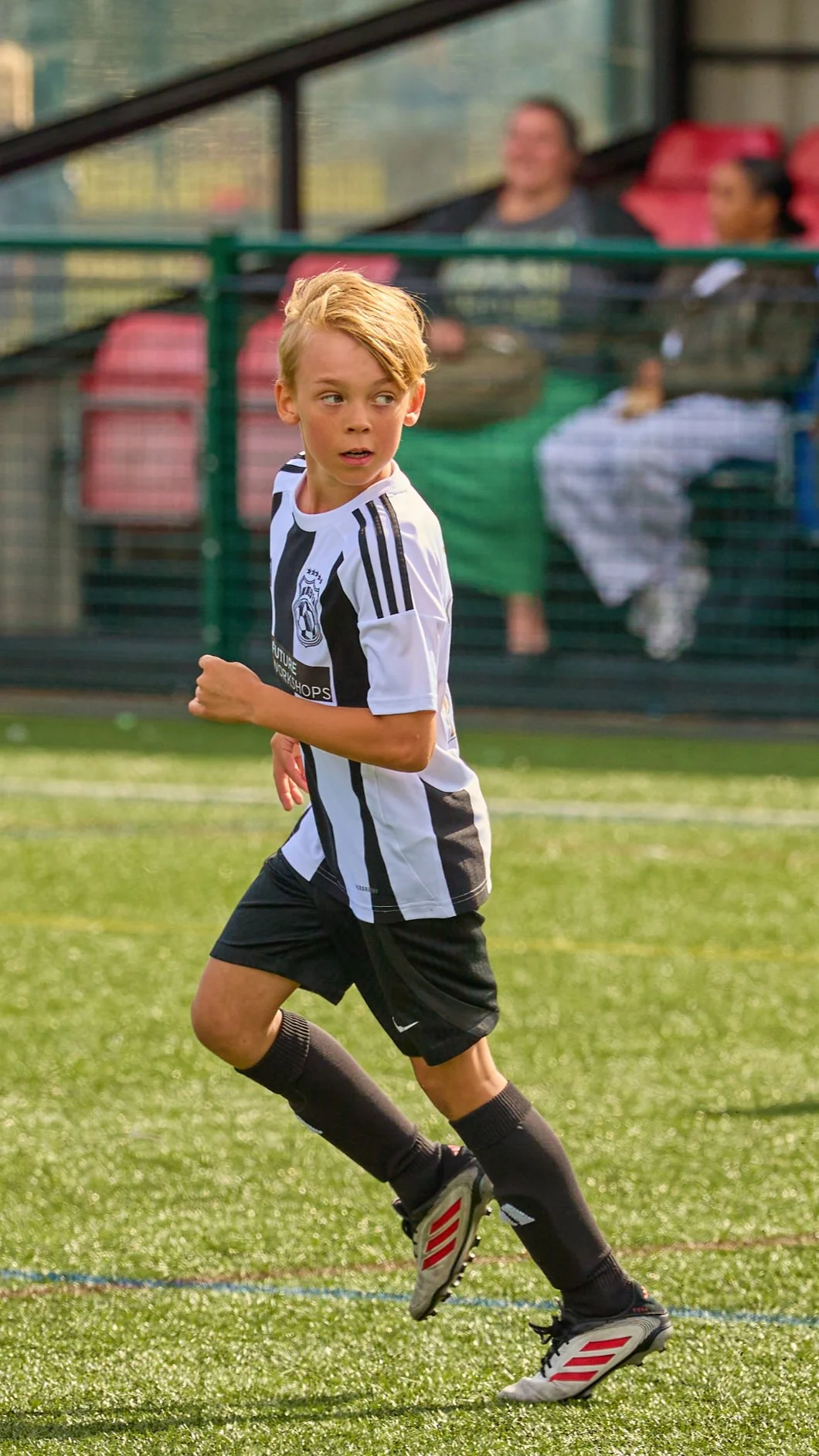 A young boy playing soccer on a field, wearing a black and white striped jersey, black shorts, and black knee-high socks.