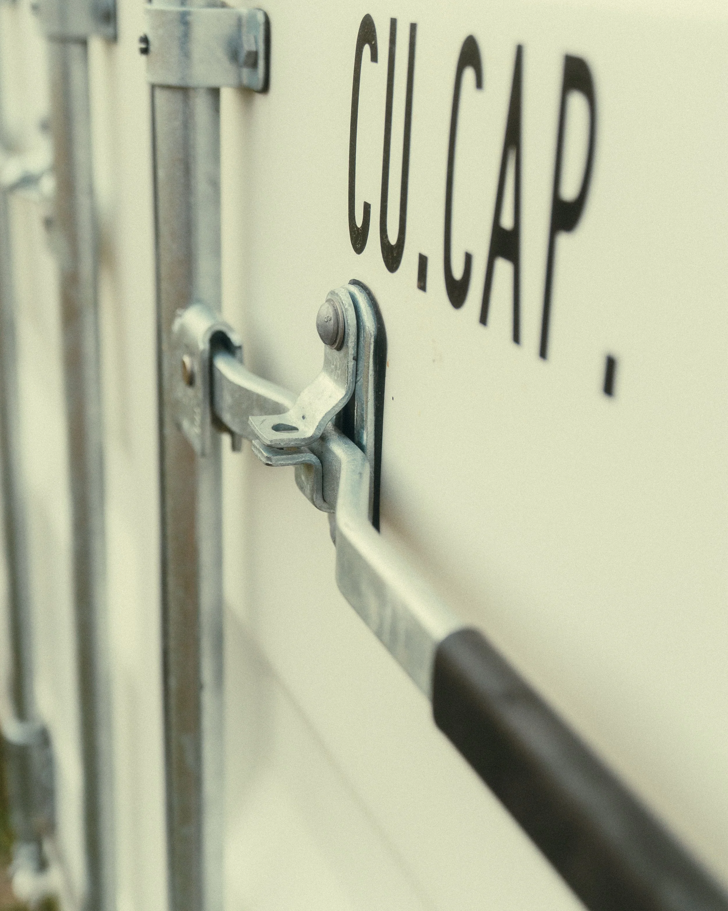 Close-up of a mechanical locking mechanism on a white metal door with the text 'C.O. C.A.P.' printed on it.