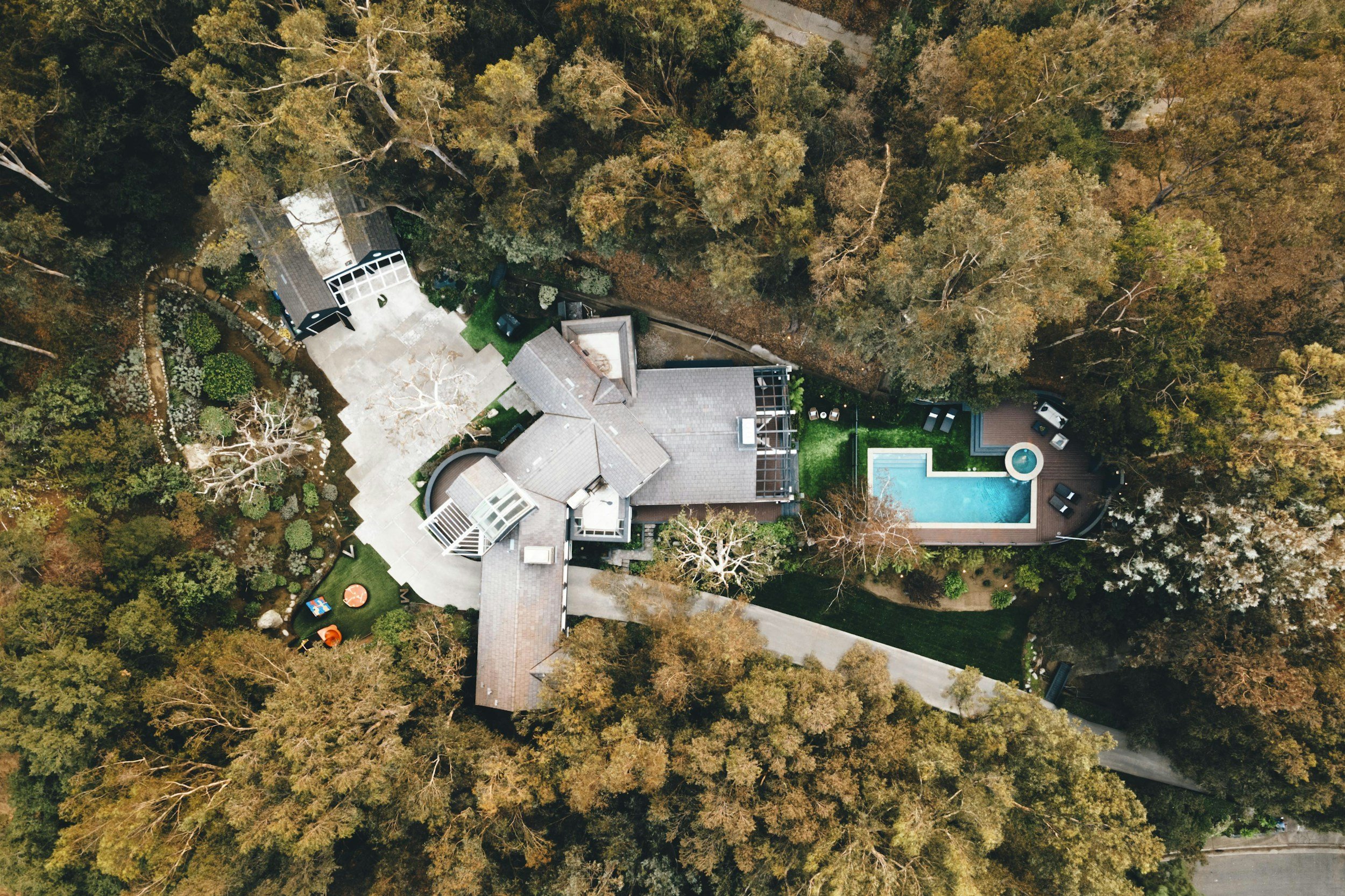 Aerial view of a house surrounded by trees with a swimming pool and backyard deck.
