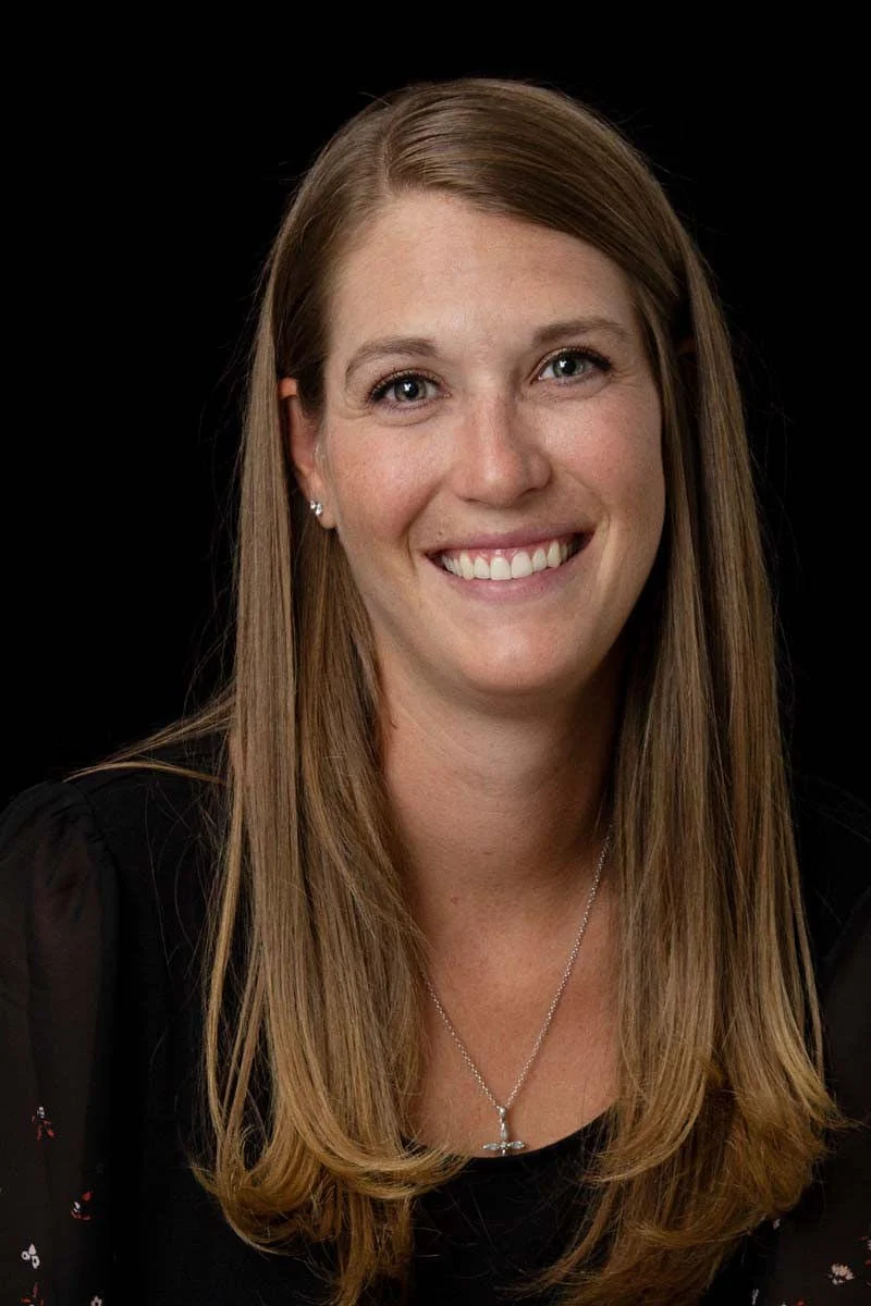 Smiling woman with brown hair in front of a black background
