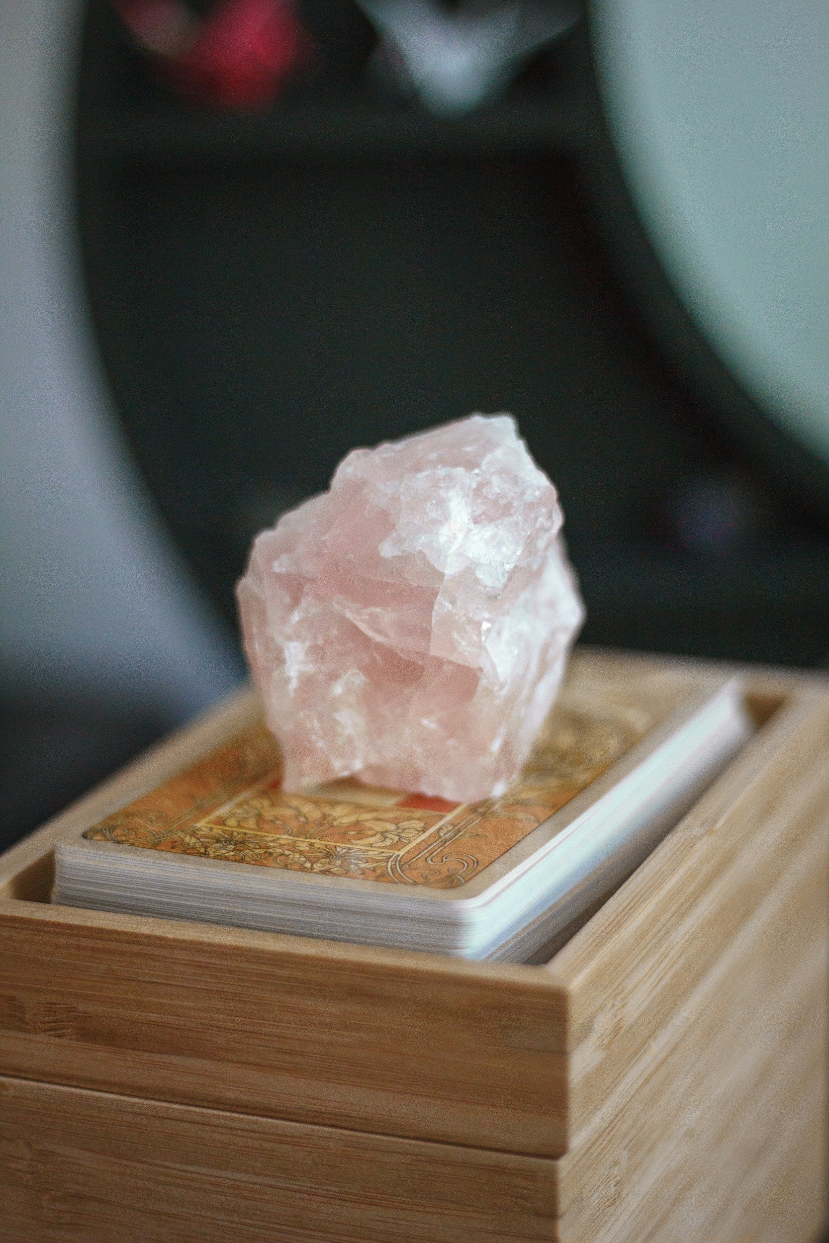 A pink Himalayan salt crystal resting on a deck of tarot cards, placed inside a wooden box.