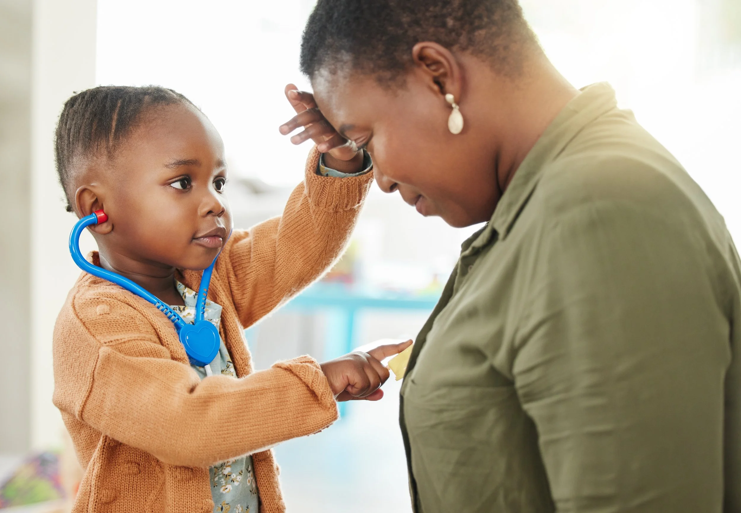 A young child uses a toy stethoscope to play doctor with her mom, highlighting the power of pretend play in early learning and family engagement.