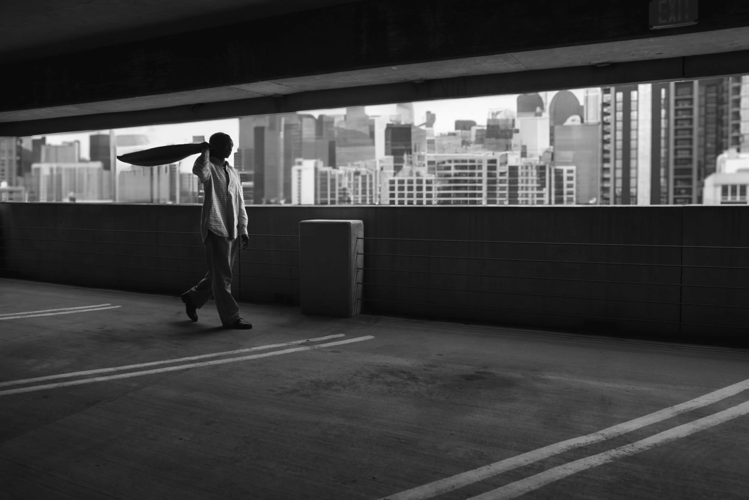 A silhouette of a person walking in an urban parking garage with city skyscrapers in the background.