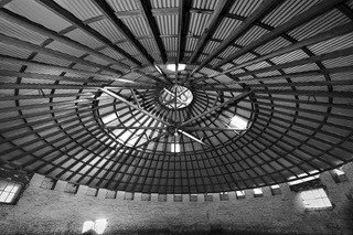 Interior view of a large circular industrial ceiling with metal beams and a central light fixture.