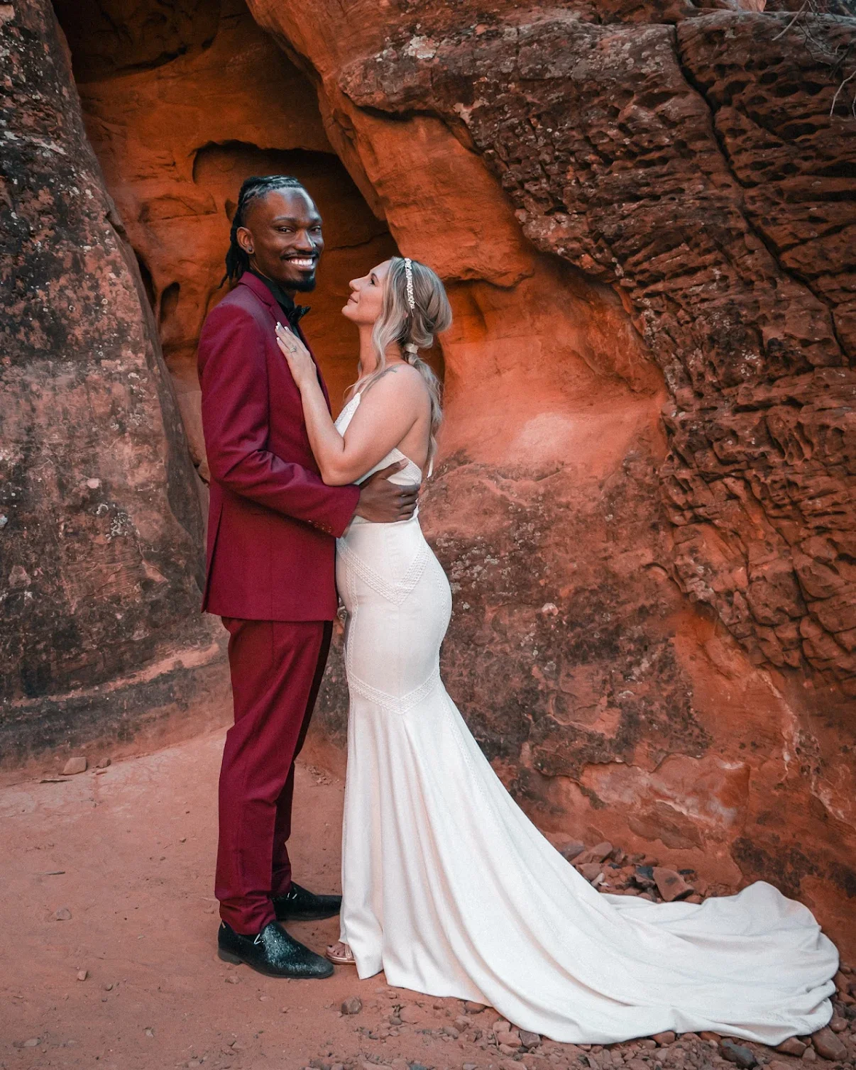 A newlywed couple stands close together in a red rock canyon, dressed in wedding attire, sharing an intimate moment.