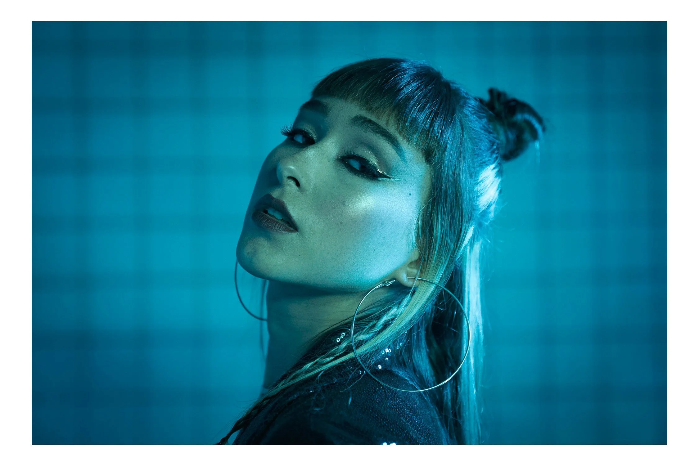 Woman with dark hair in two buns and bangs, lit in deep teal blue