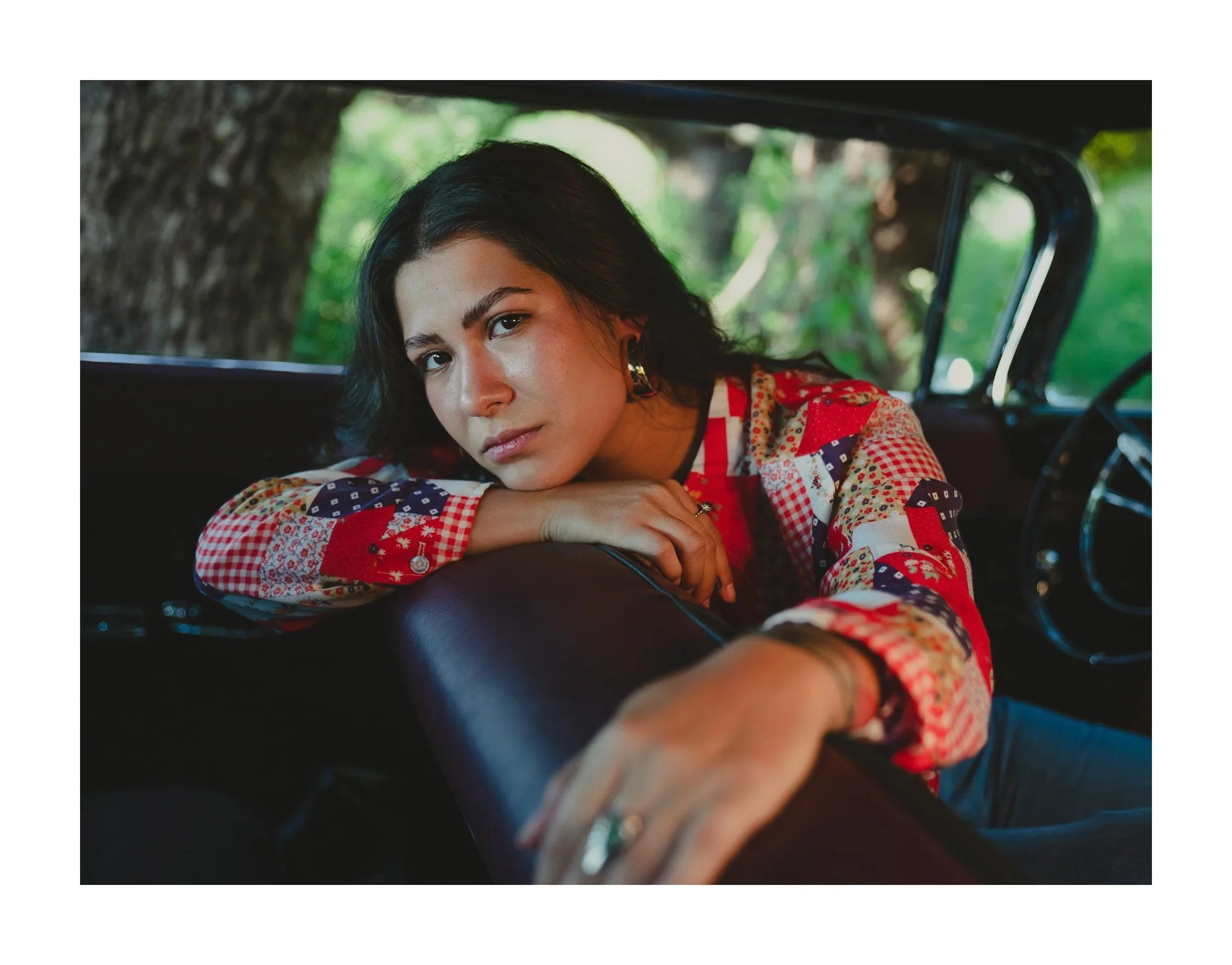 Woman with dark hair in a red and white patterned shirt leaning across a car seat
