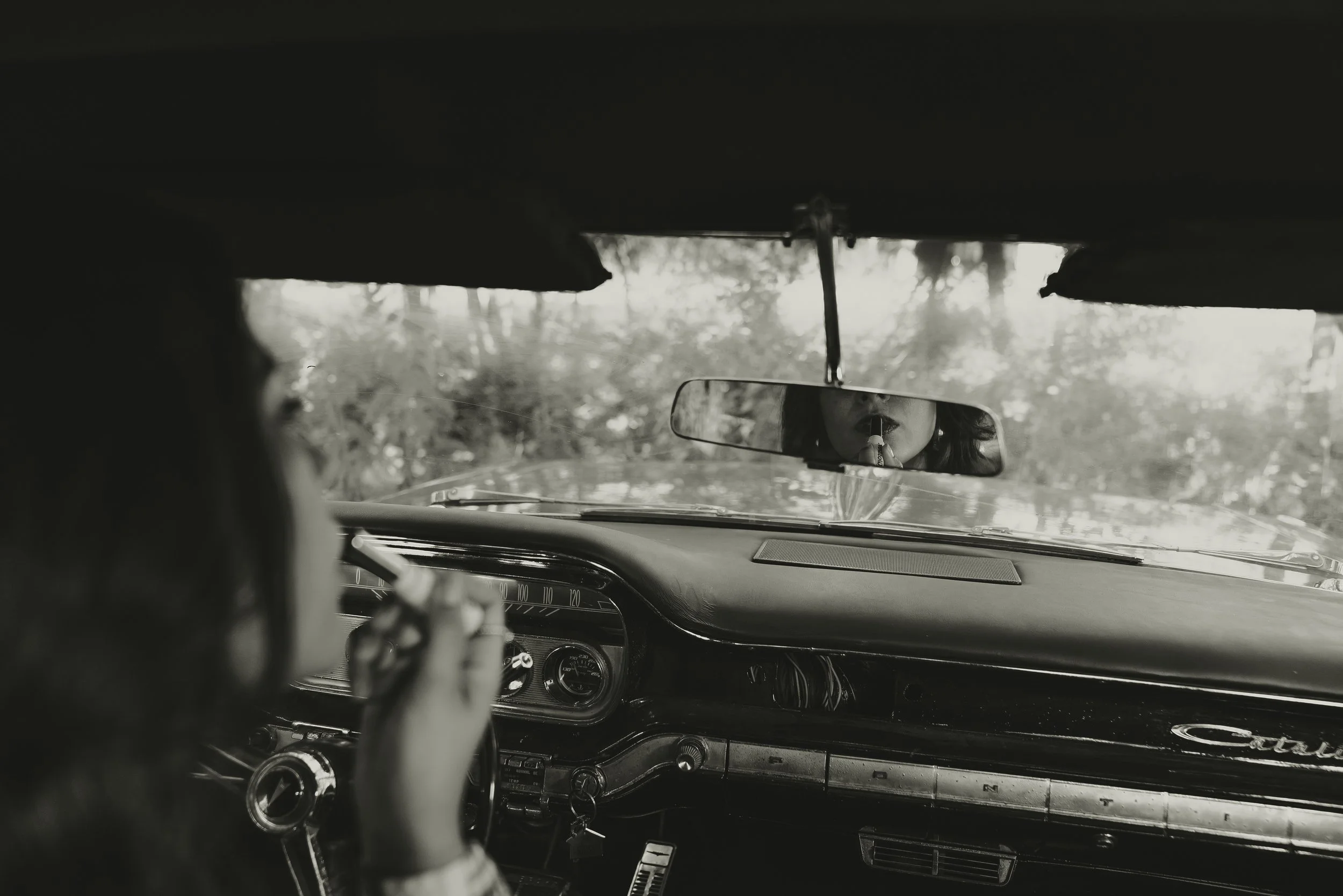 Black and white view over a driver's shoulder toward a vintage car dashboard