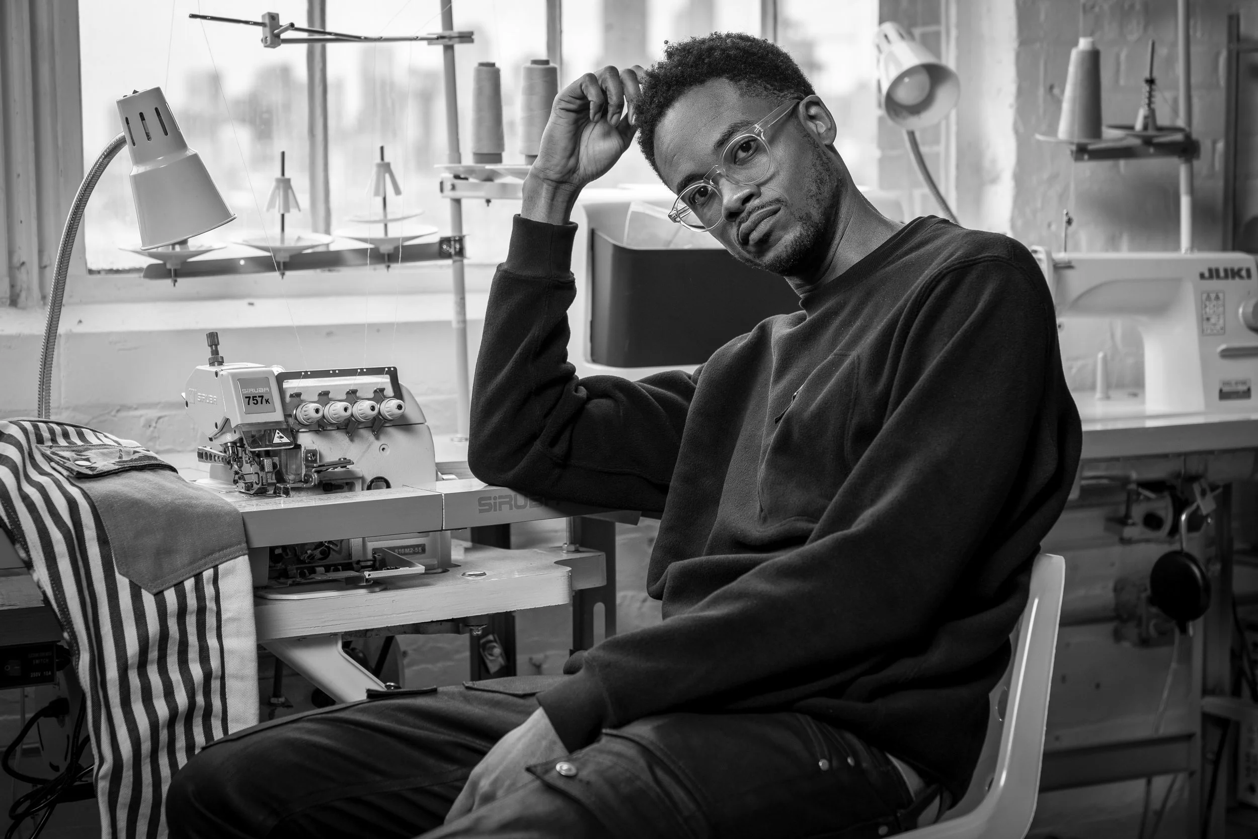 Black and white portrait of a man in glasses and a dark sweater in a workshop