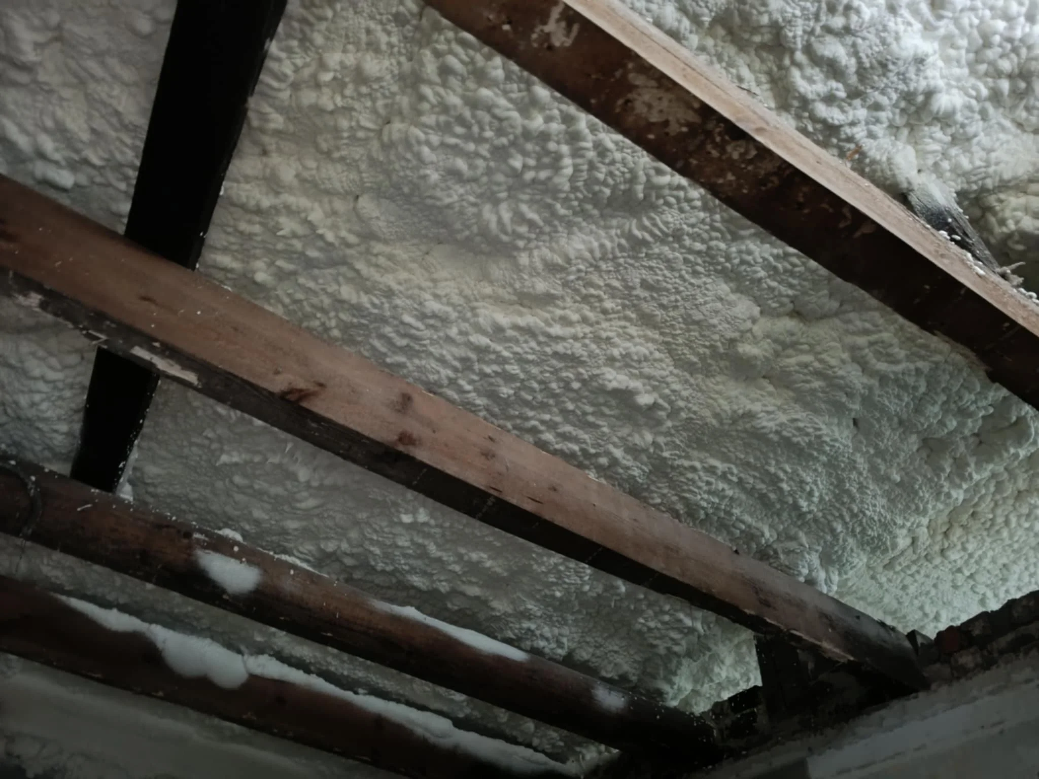 Ceiling insulation with wooden beams and spray foam insulation between them.