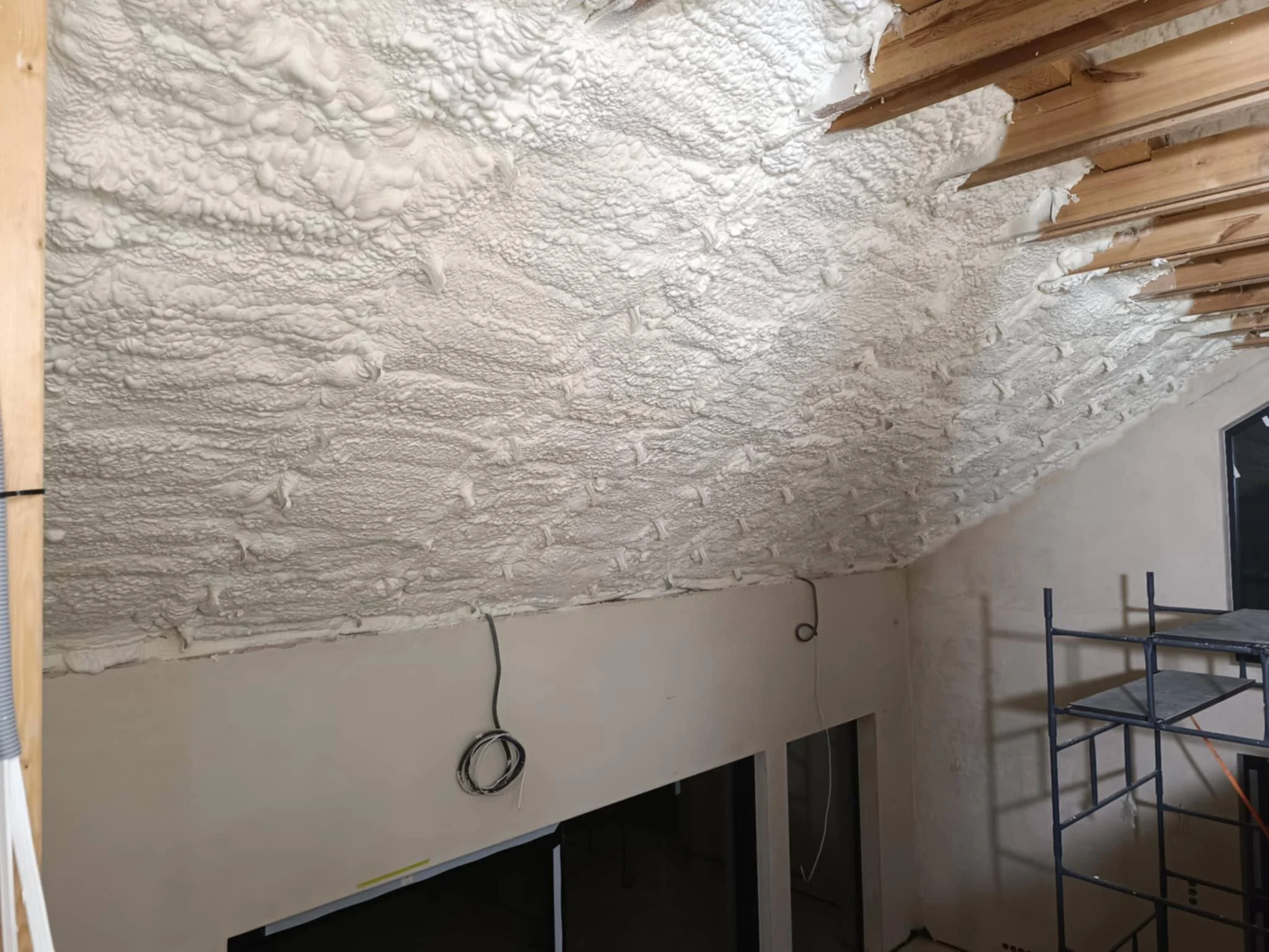 Construction site with insulation spray foam on ceiling and exposed wooden beams.
