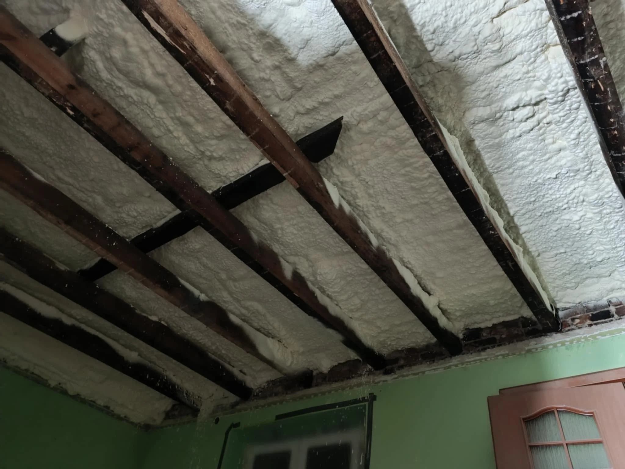 Ceiling with exposed dark brown wooden beams and spray foam insulation.