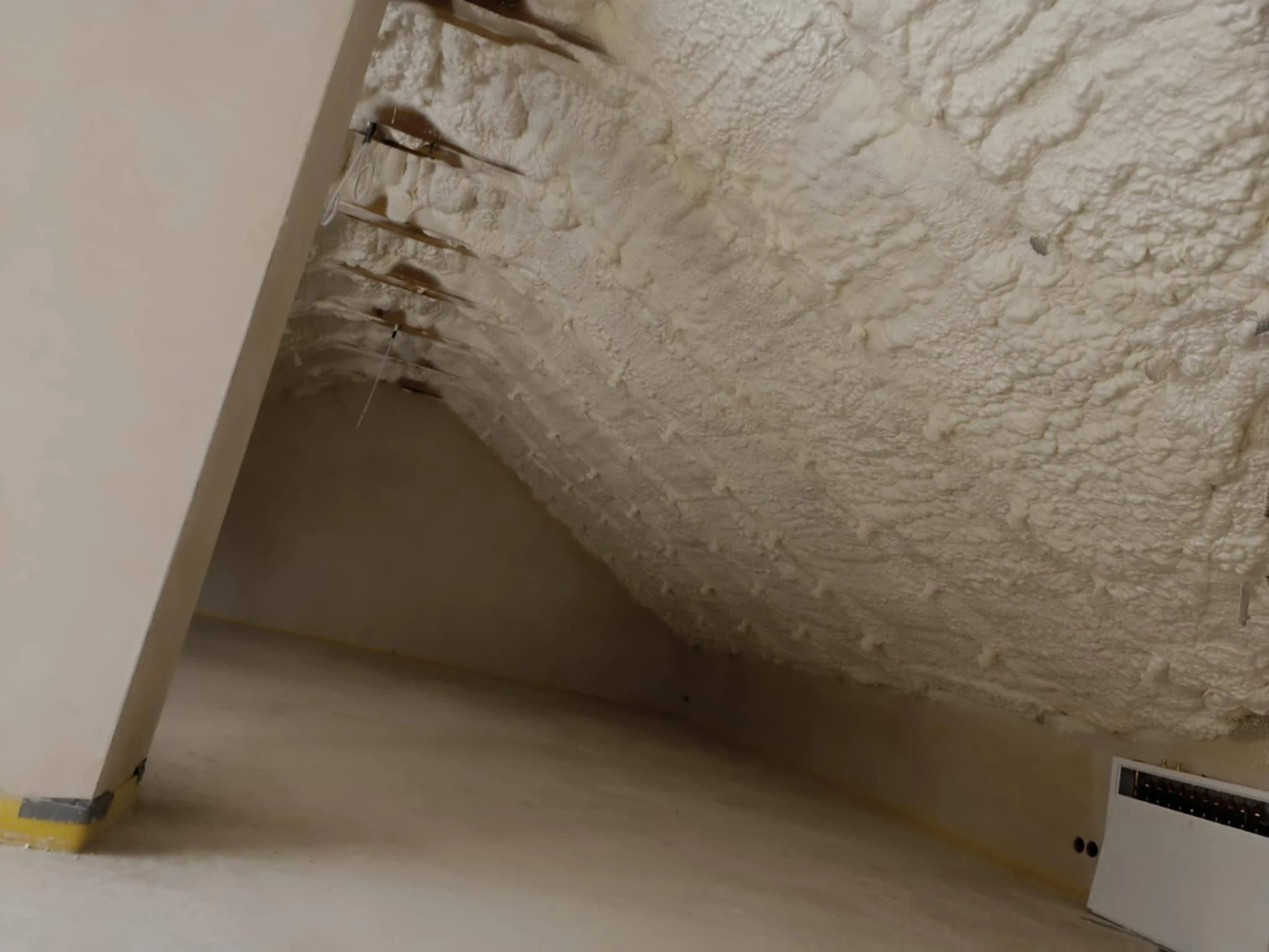 A ceiling with spray foam insulation and a corner of an unfinished room, with some wiring and electrical outlets visible.