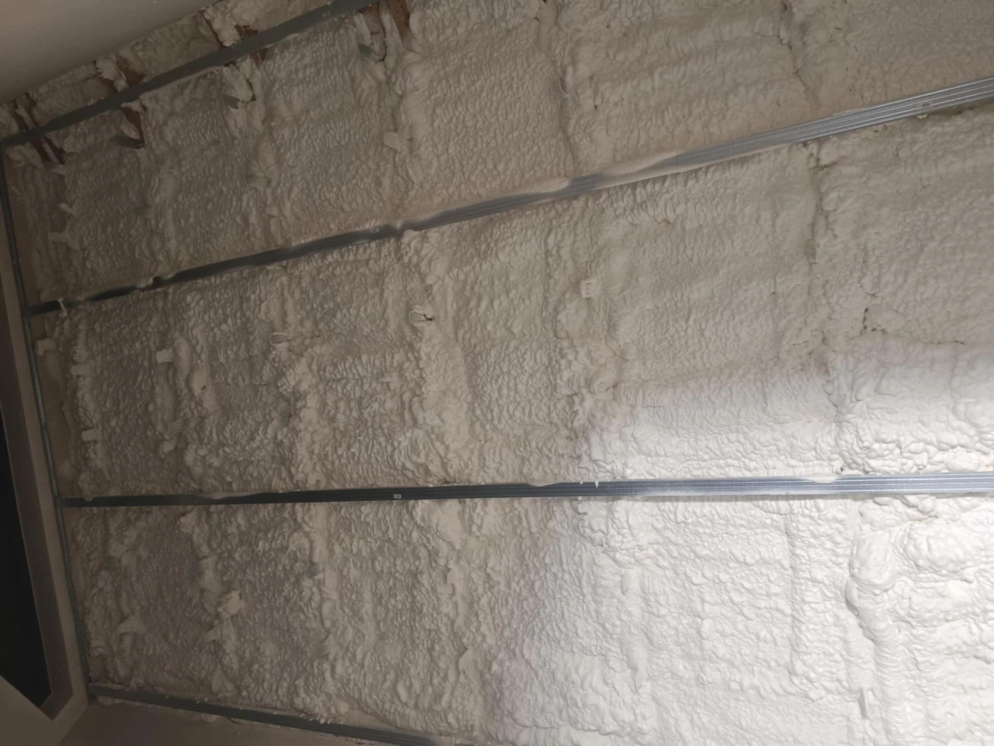 Insulation foam sprayed on wall between metal framing studs in construction process.