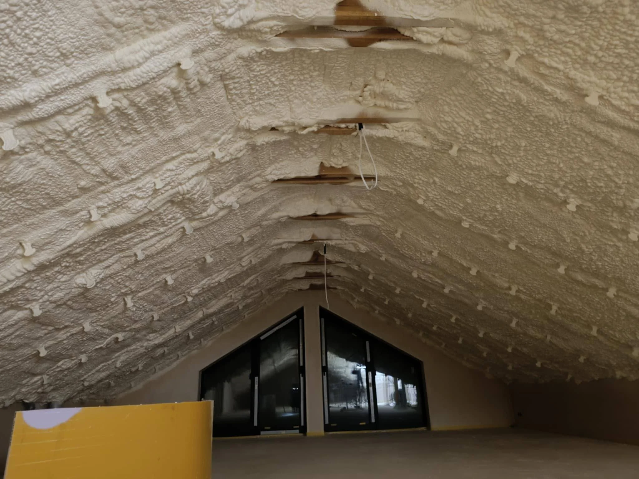 Pianka izolacyjna natryskiwana na dach poddasza wewnątrz domu, z widocznymi poniżej oknami.