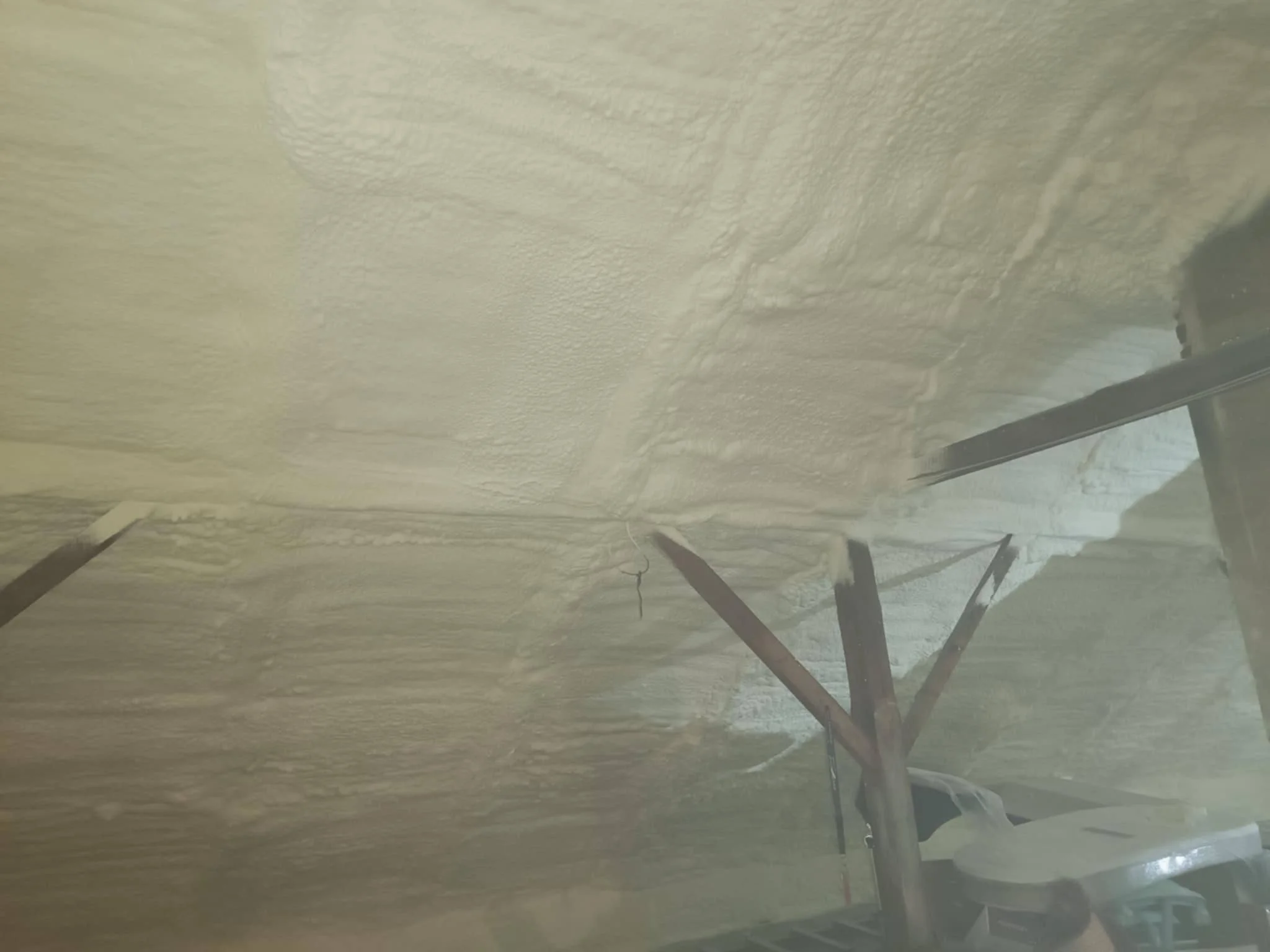 Insulation foam on a ceiling with support beams and a ladder visible.