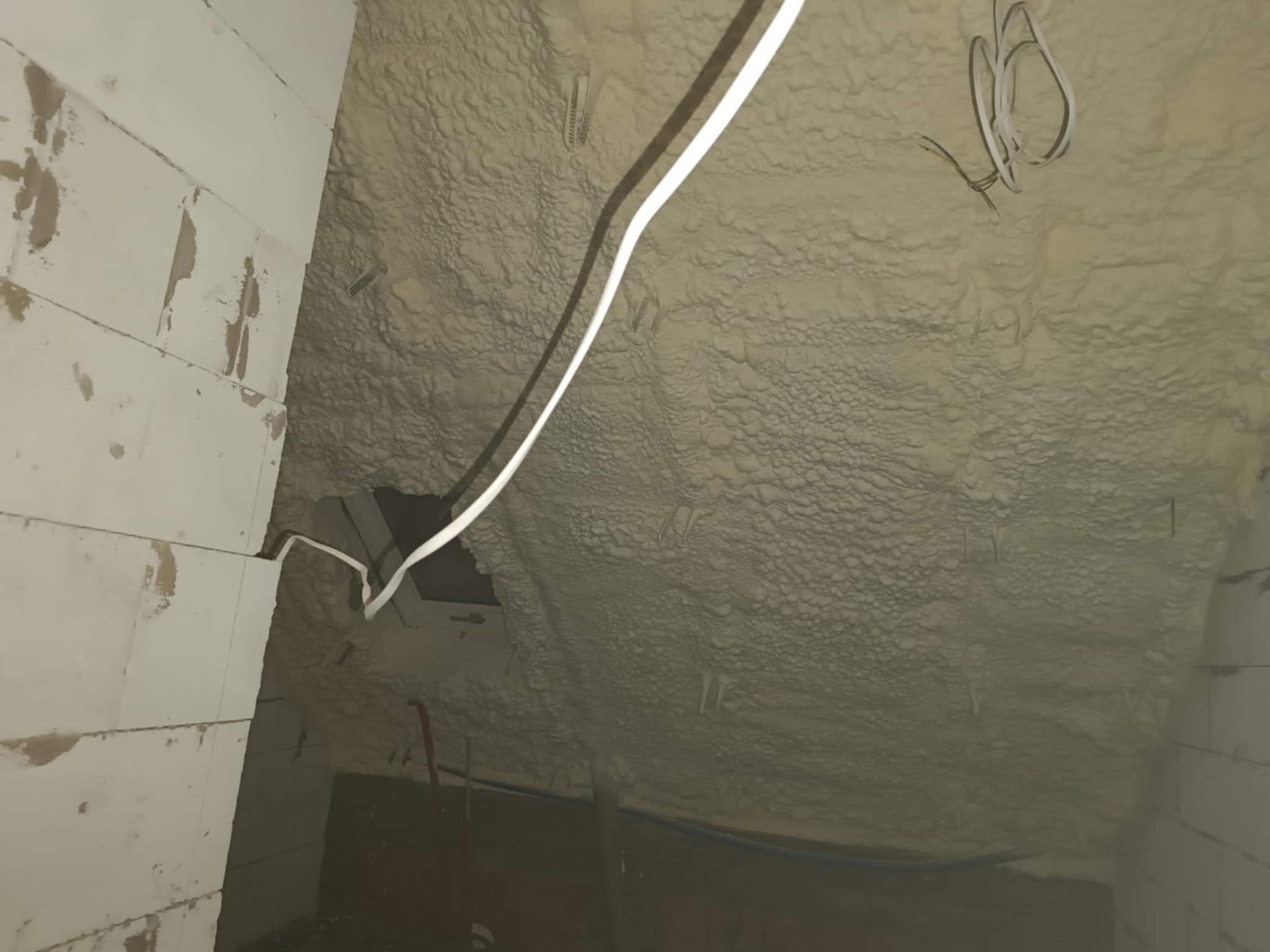 Ceiling under construction with spray foam insulation, exposed wirings, and partially finished walls.