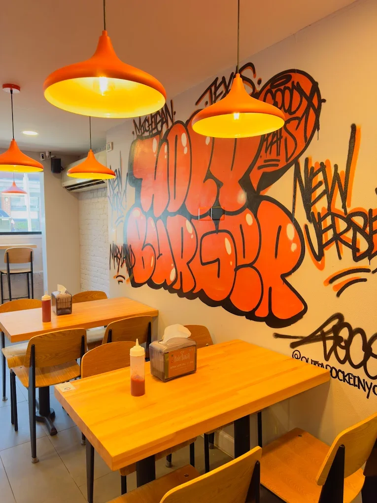 Neon sign reading 'Holy Burger' inside a restaurant, visible through a window at night.