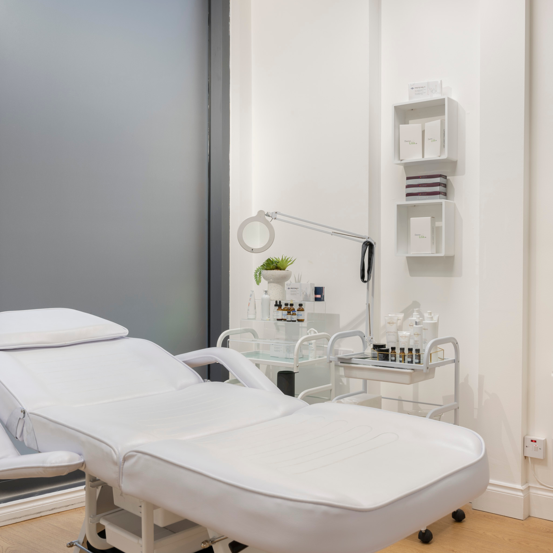 Medical examination room with a white treatment bed, medical equipment, and supplies on a cart and shelves.