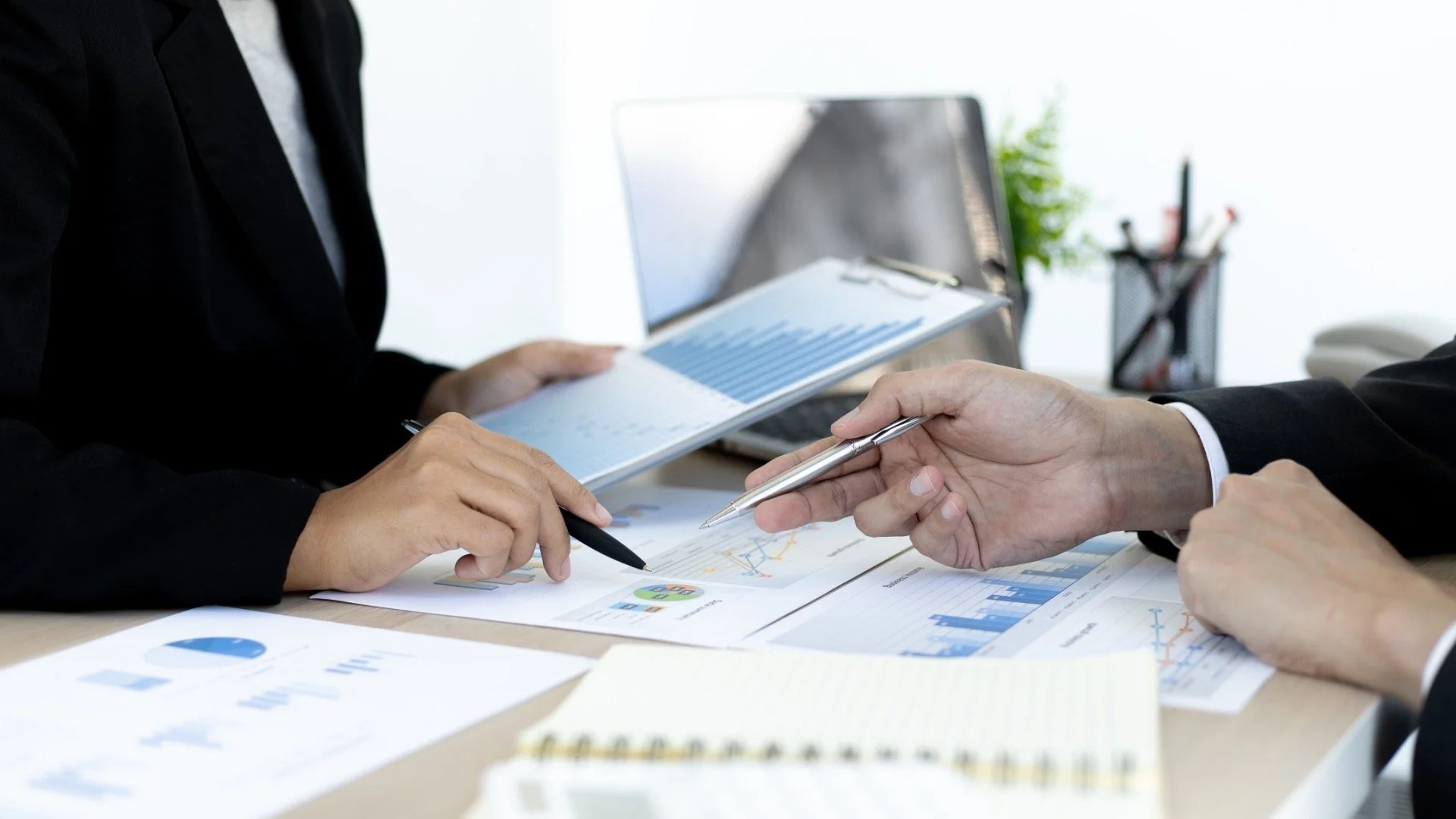 Two people in business attire reviewing financial charts and graphs during a meeting at a desk.
