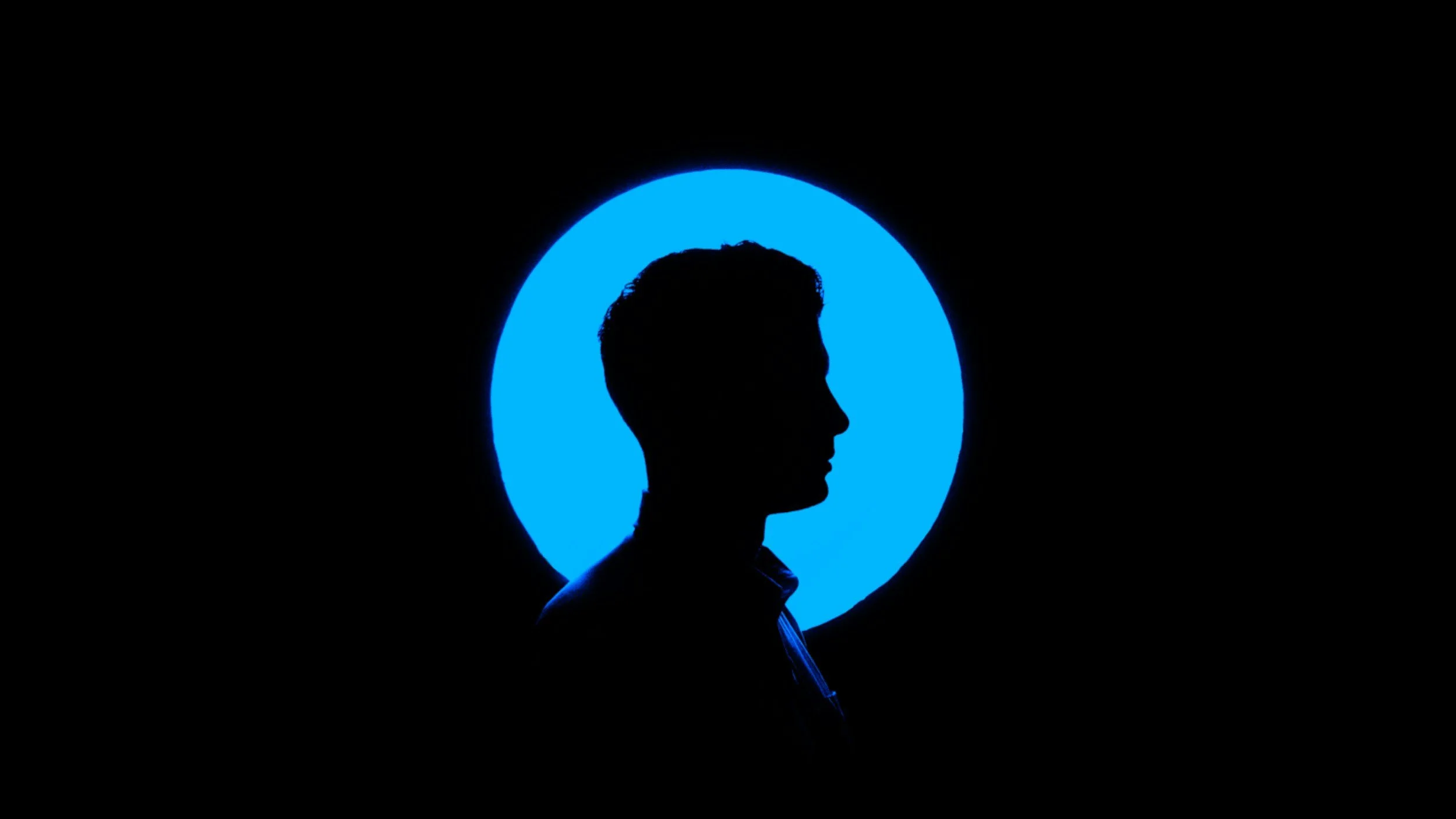 Silhouette of a man's profile in front of a blue glowing circle on a black background.