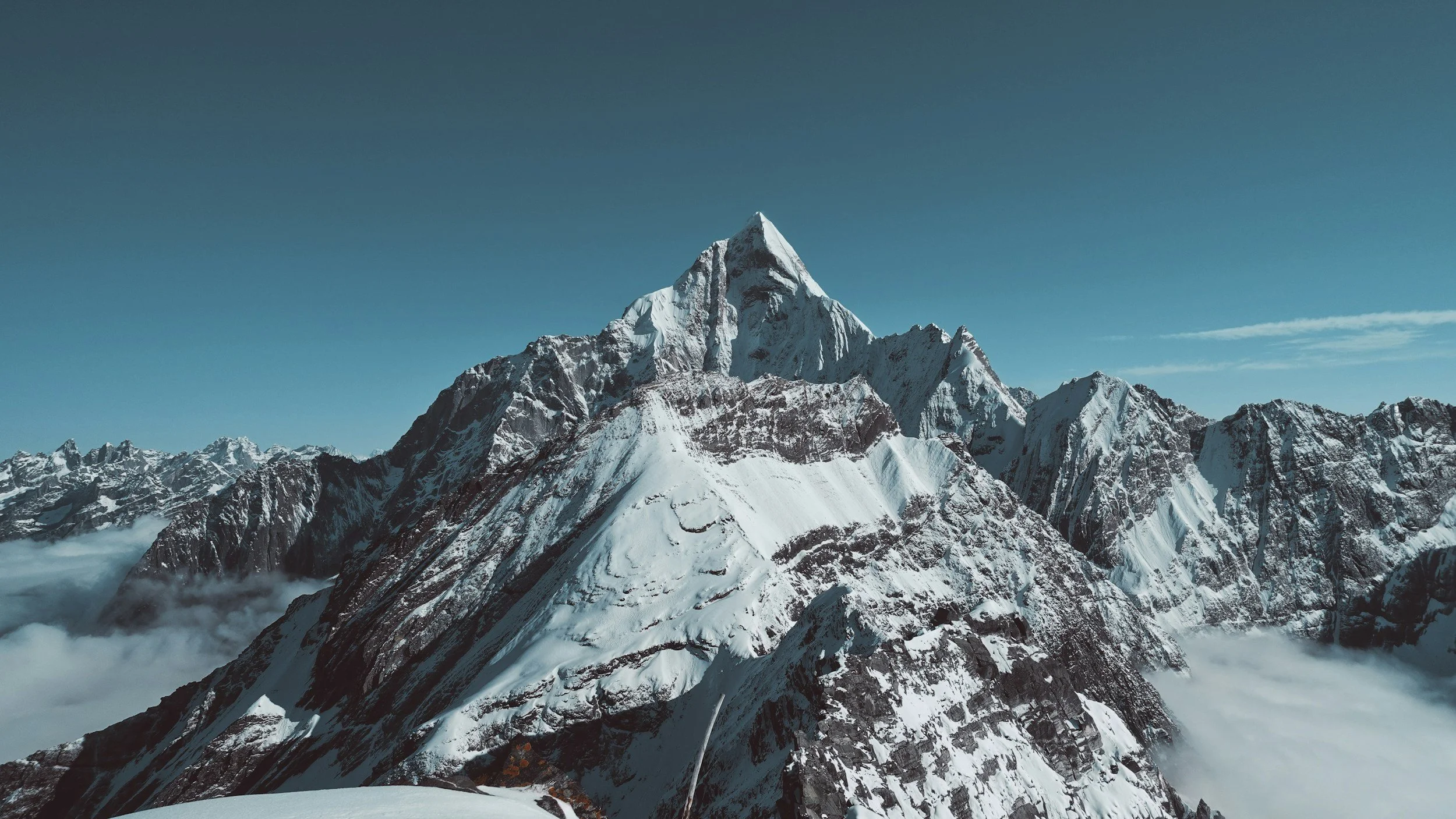 Snow-covered mountain peaks above a sea of clouds under a blue sky.