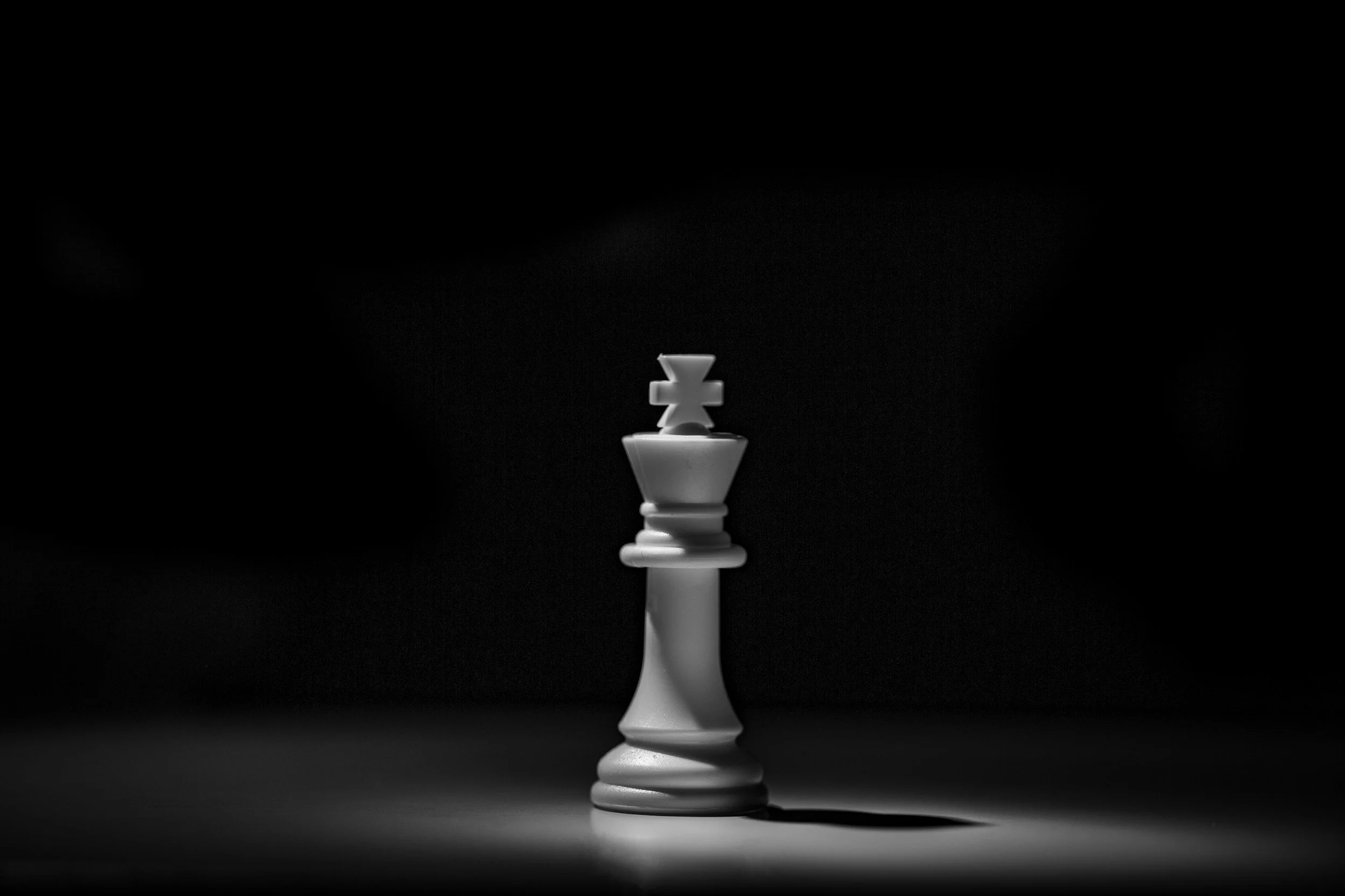 A single white king chess piece on a dark background with a shadow extending to the right.