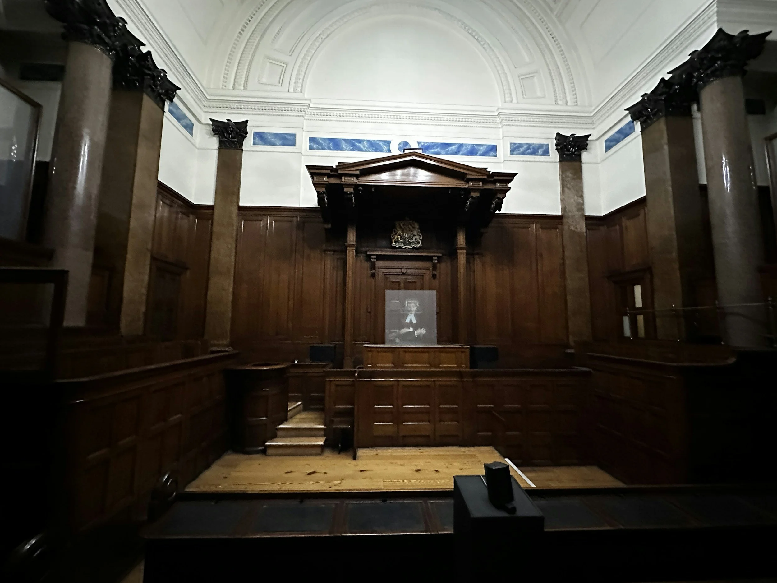 Historical courtroom with wooden paneling, columns, and a portrait of Abraham Lincoln.