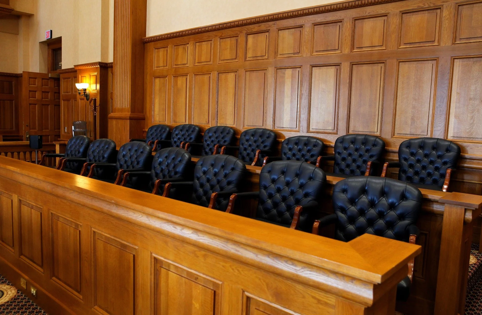 Empty courtroom with black leather chairs arranged in rows and wooden paneling on the walls.