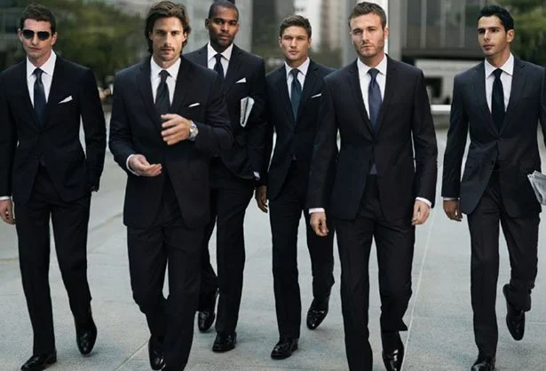 Six men in business suits walking outdoors in an urban area.