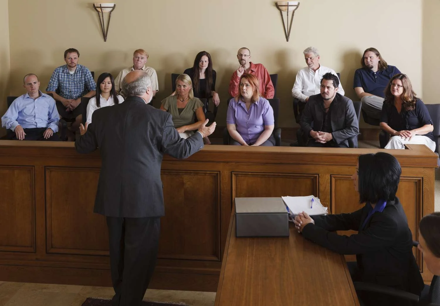 A courtroom scene with a judge and a lawyer speaking to a jury of twelve people.