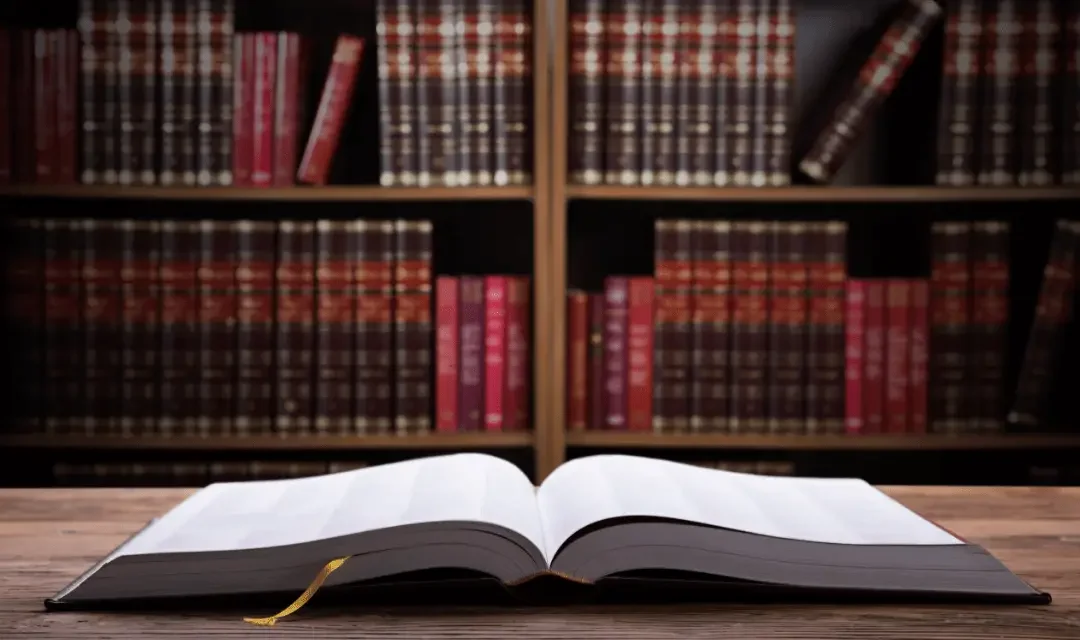 Open book on a wooden table with library shelves filled with books in the background.