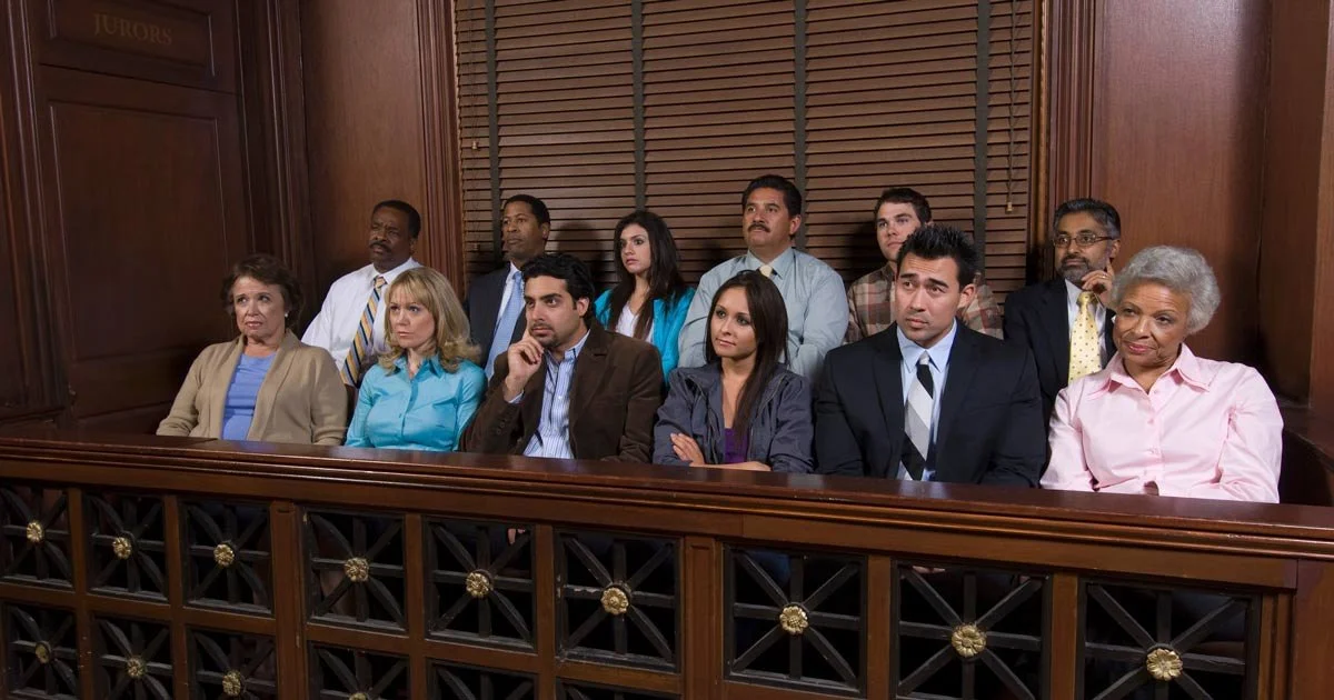People sitting in a courtroom, listening attentively, with wood-paneled walls and judge's bench behind them.