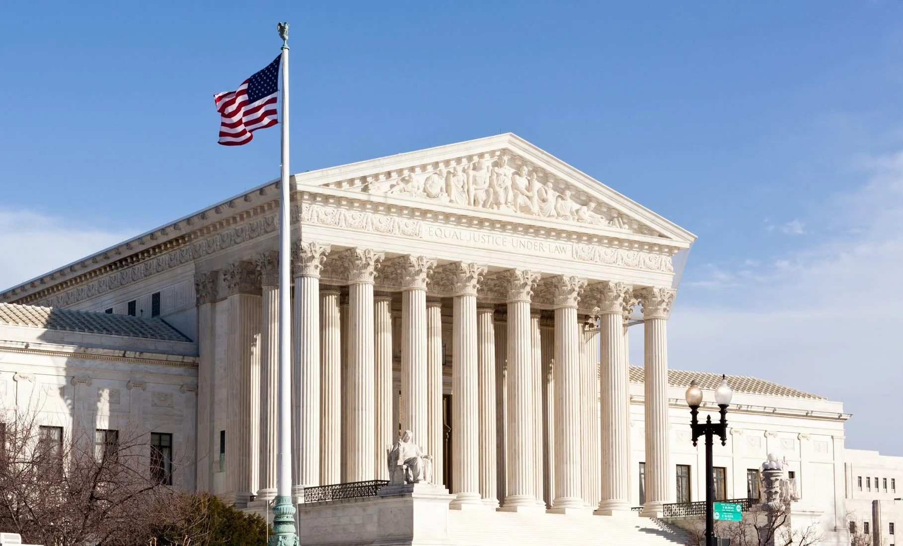 U.S. Supreme Court building with American flag flying in front, clear blue sky.