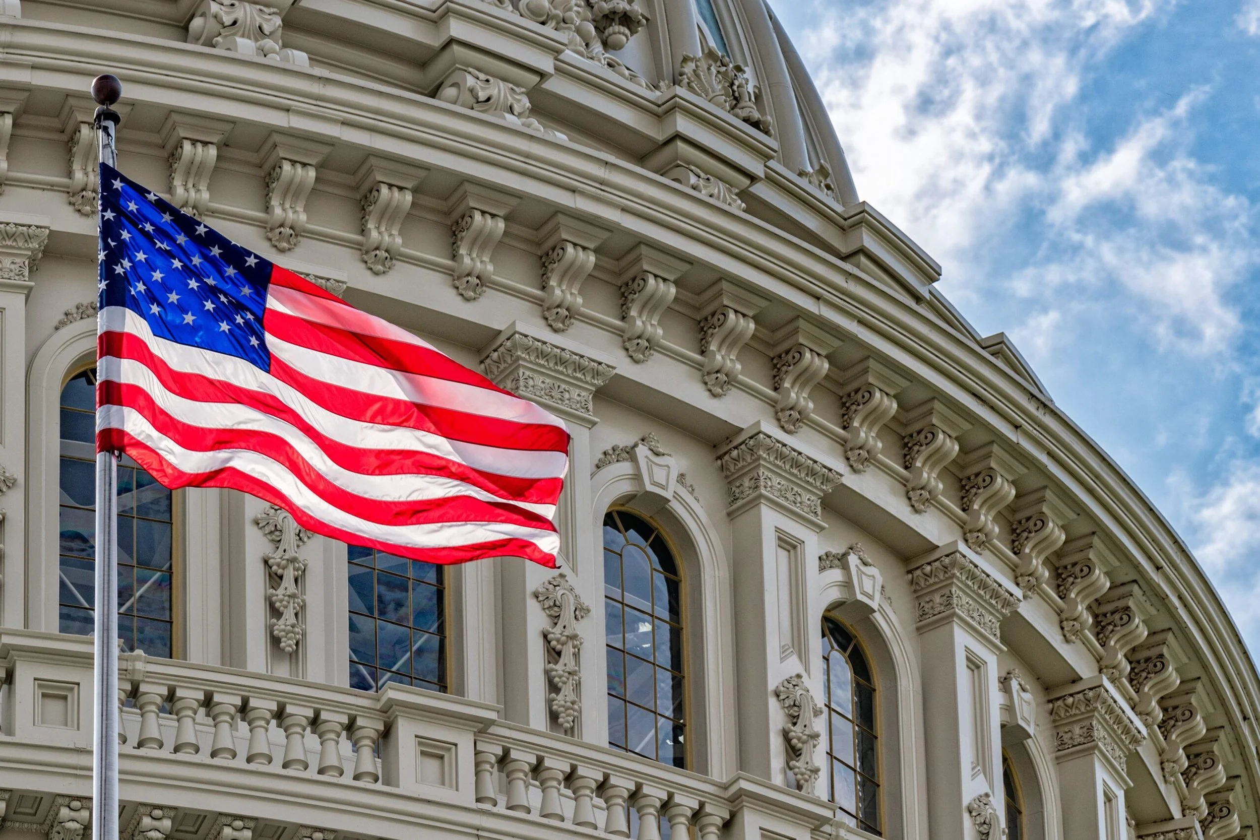 The American flag flying outside a historic government building with ornate architectural details and a blue sky with clouds.