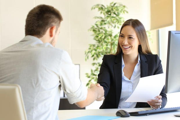A woman in business attire shaking hands with a man during a professional meeting in an office.