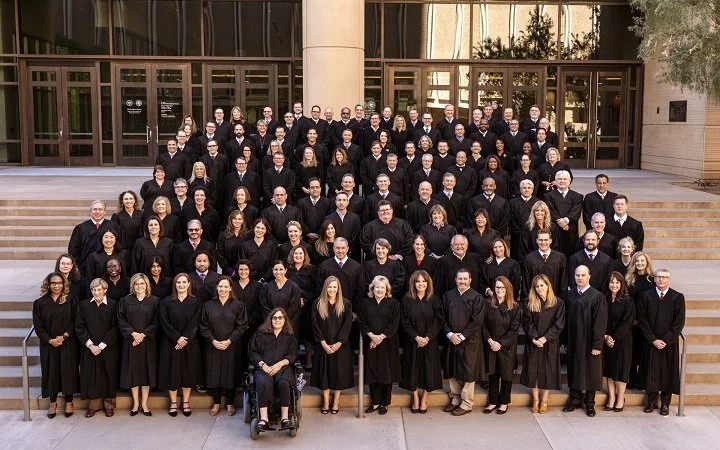 Group of people in graduation gowns and caps standing on the steps in front of a building.