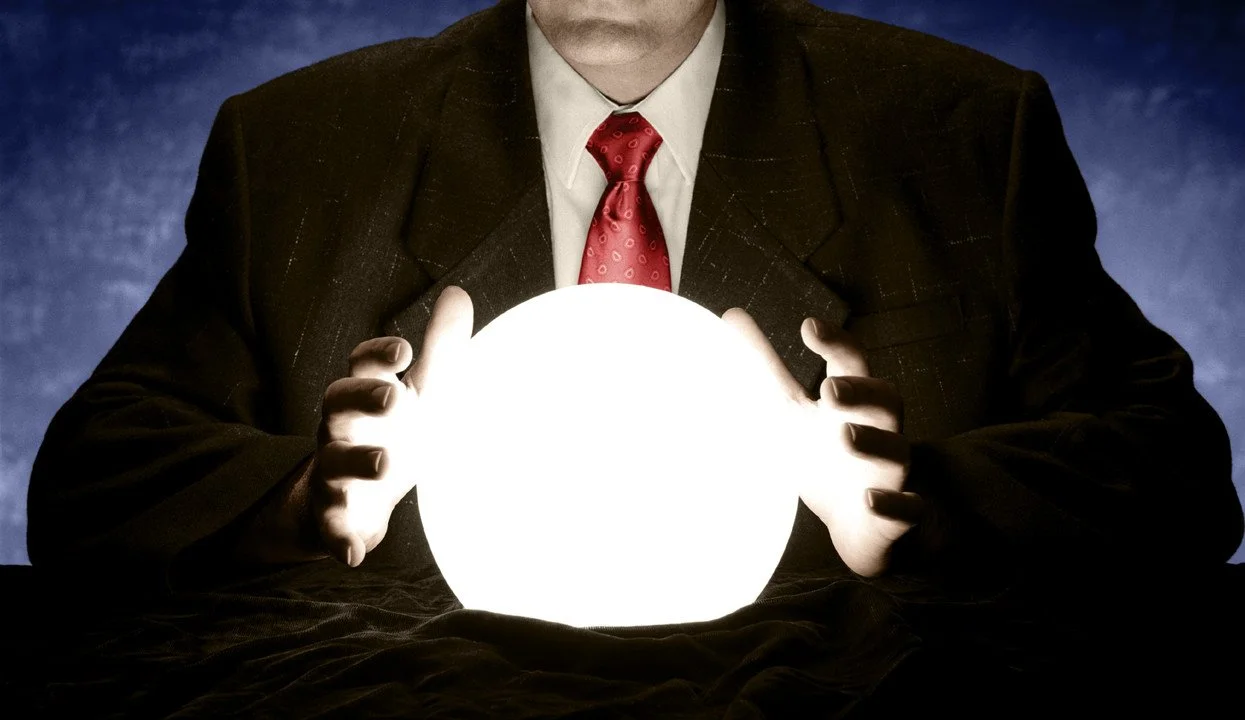 A man in a suit and red tie holding a glowing orb with both hands against a dark background.